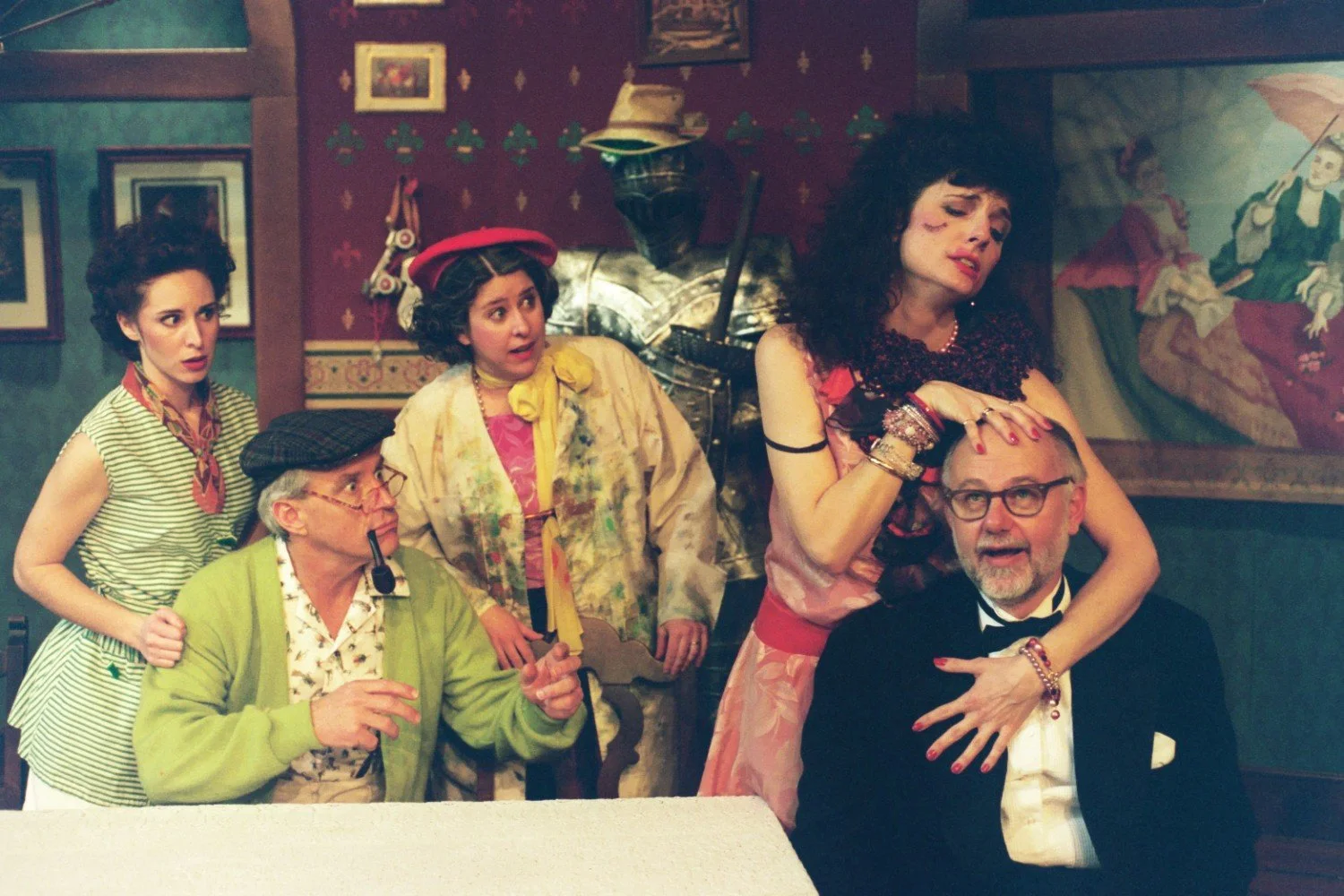 A group of five people in eccentric vintage clothing, including a man in a tuxedo, posed dramatically in a room with eclectic décor, including a suit of armor. The expressions are theatrical and expressive.