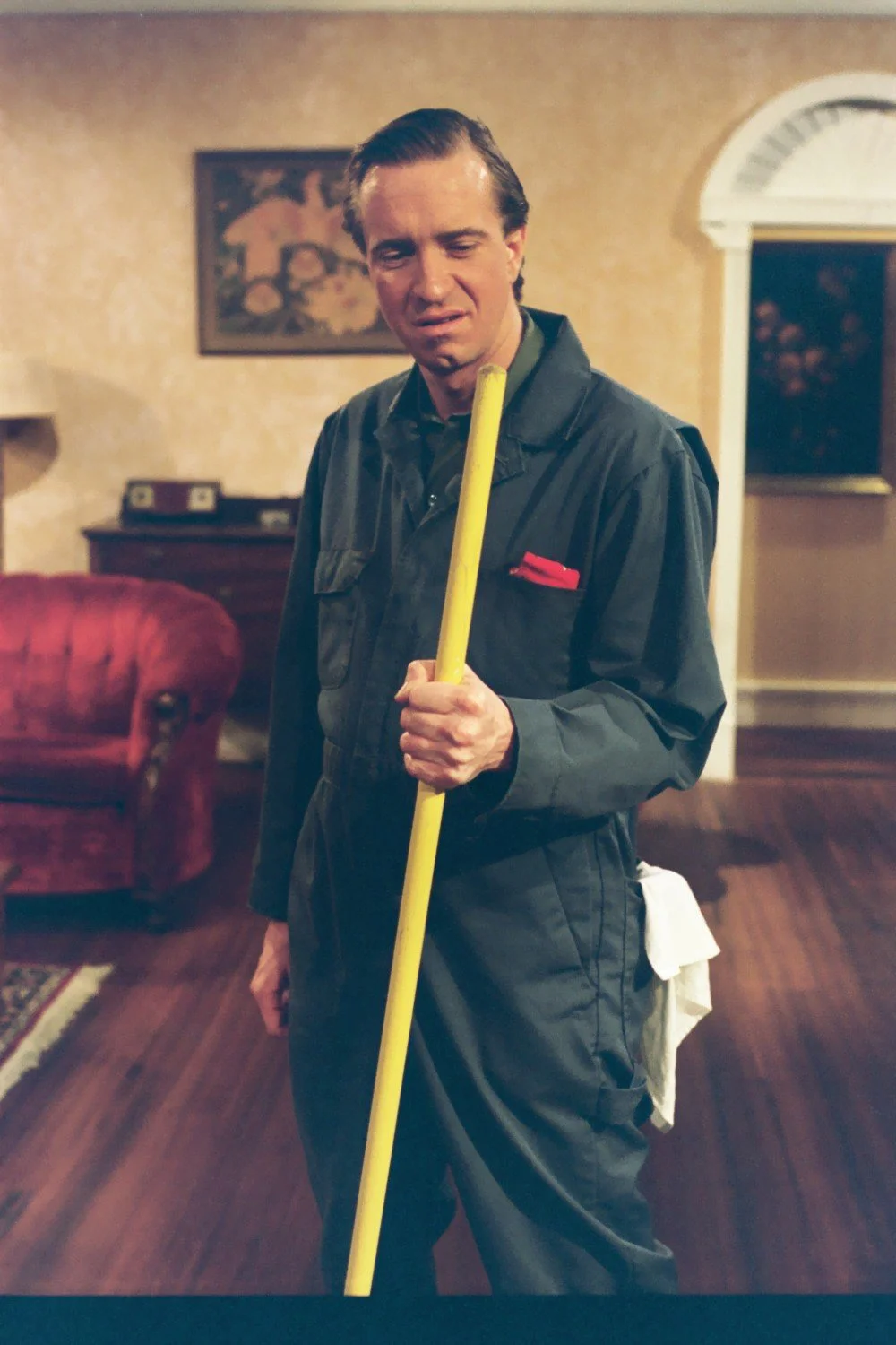 Man in work uniform holding a broom indoors