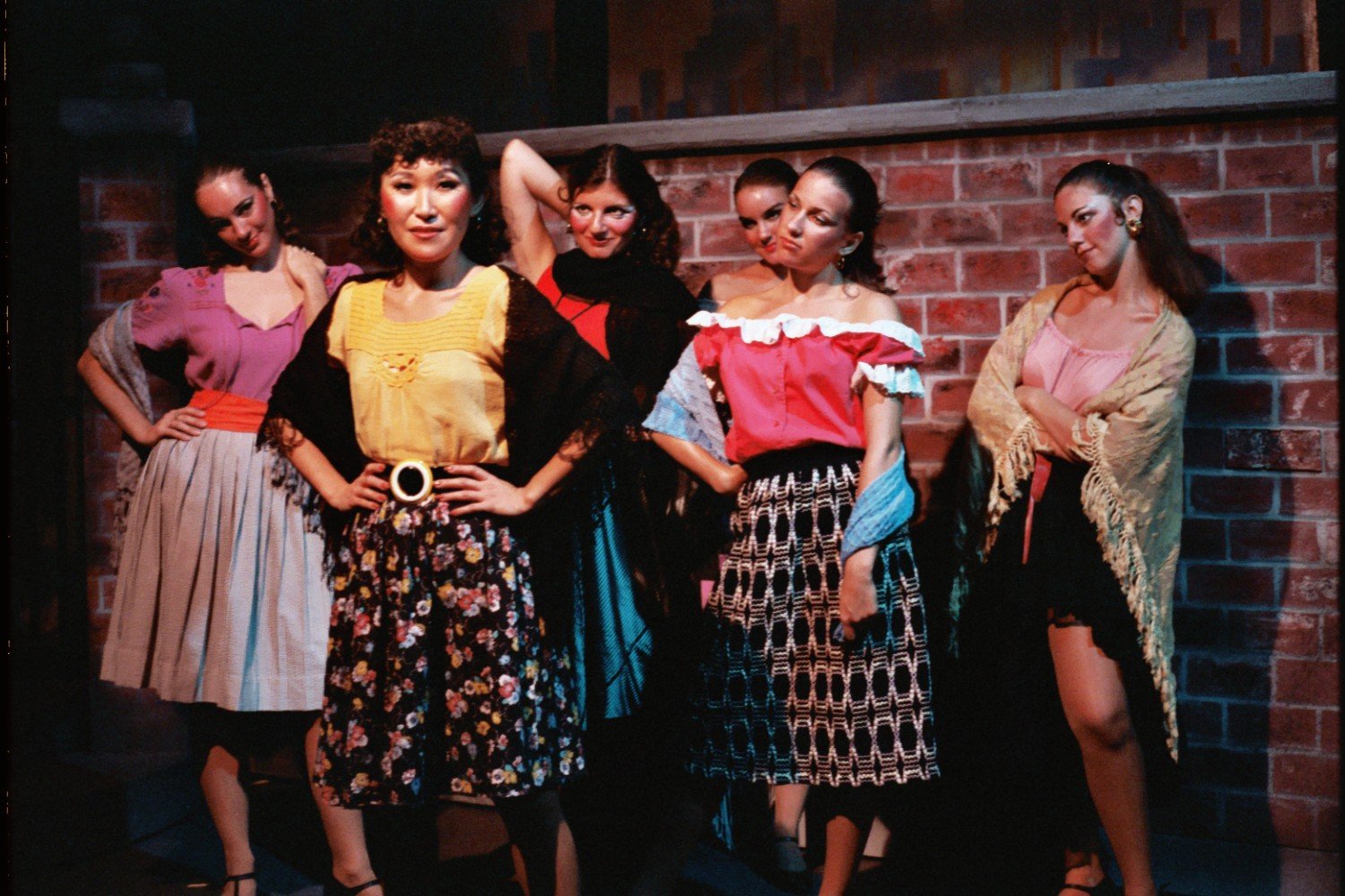 Group of women dressed in colorful, vintage-inspired outfits posing in front of a brick wall.