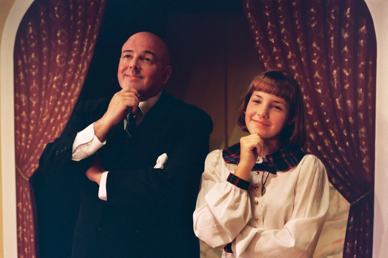 A man and a woman posing thoughtfully in front of decorative curtains.