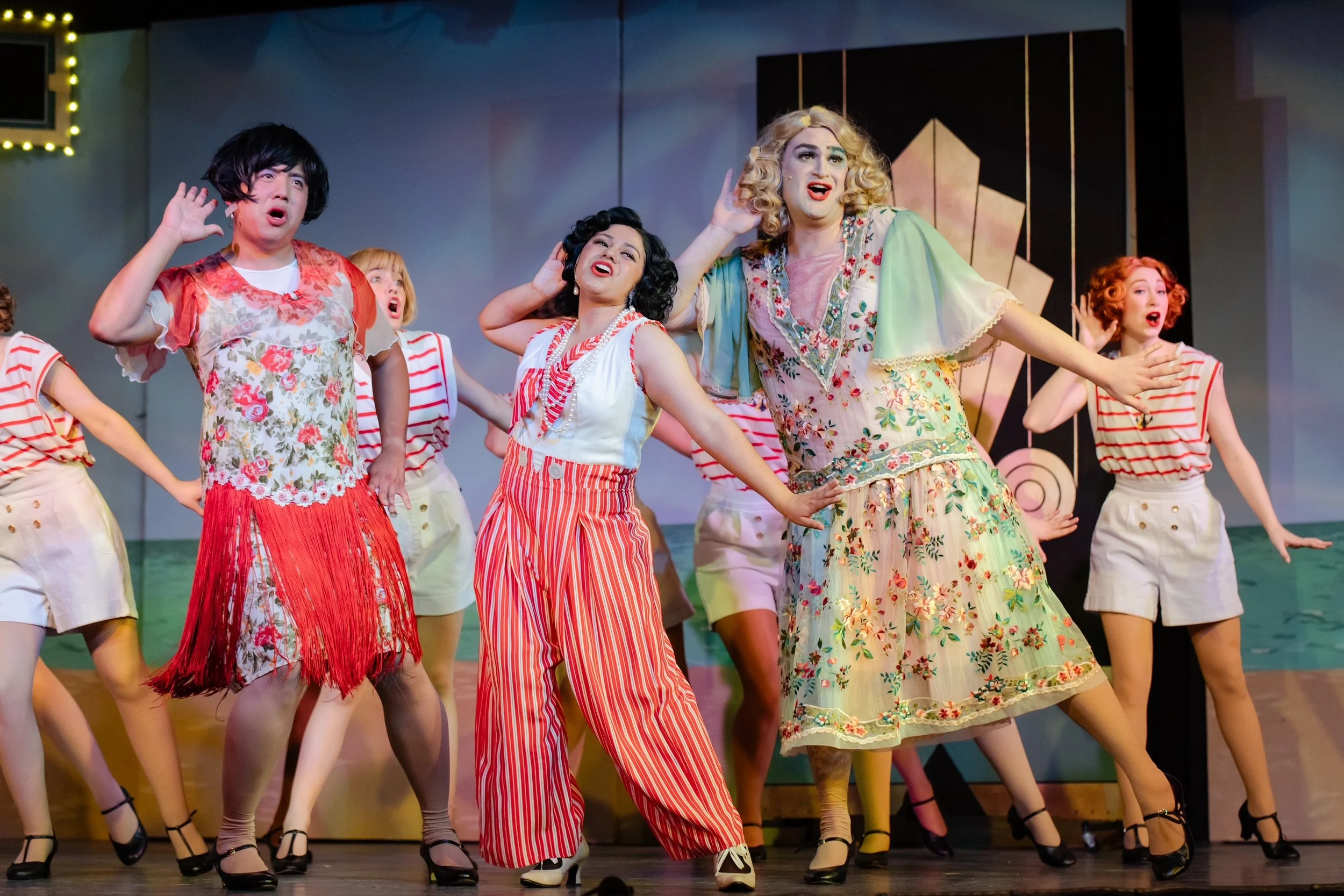 Performers in colorful vintage-style costumes on stage, singing and dancing.