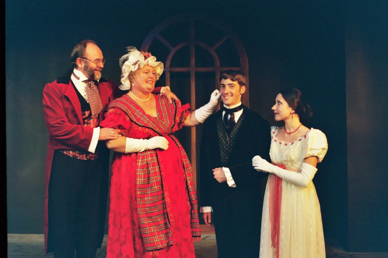 A group of four people in period costumes on stage, with two men and two women in formal attire suggestive of historical or theatrical performance.