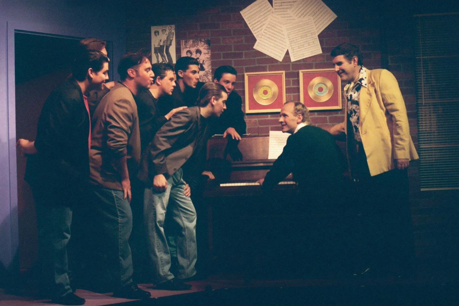 Group of people singing around a piano in a room, musical notes on the wall.