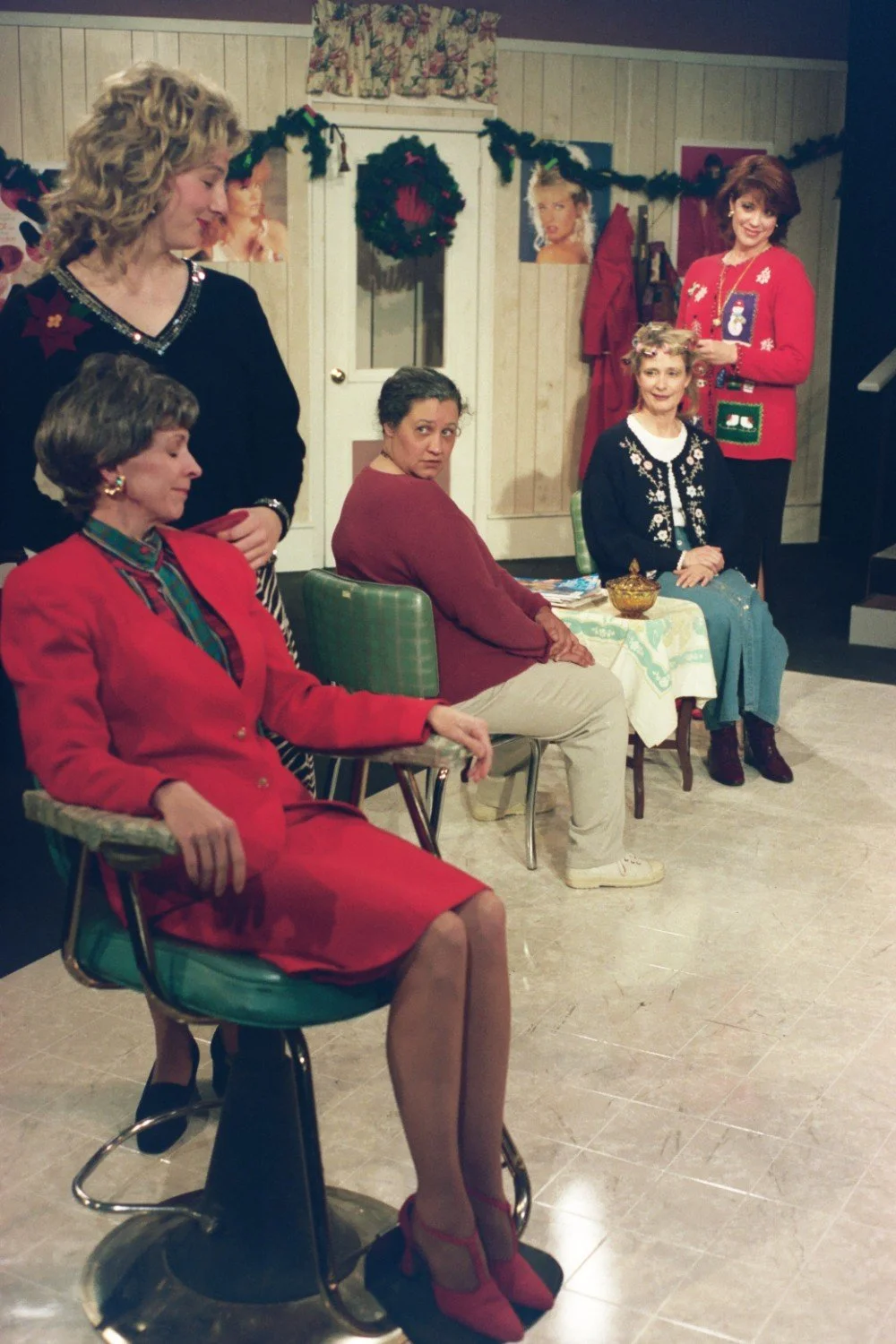 Group of women in a festive, decorated room, sitting and standing around chairs in casual and holiday attire.
