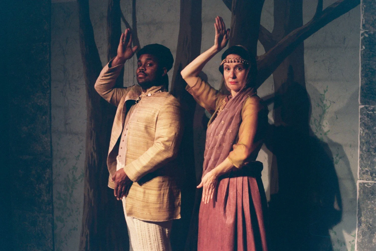 Two people posing in traditional dance costumes in front of a painted forest backdrop.