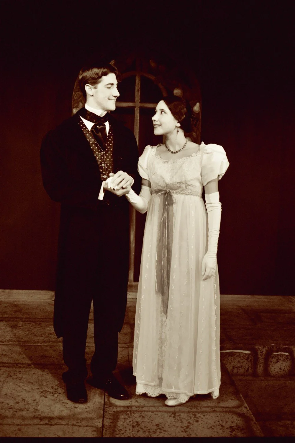 Vintage-style photo of a man and woman in formal period clothing holding hands, resembling a scene from a classic film or theater production.