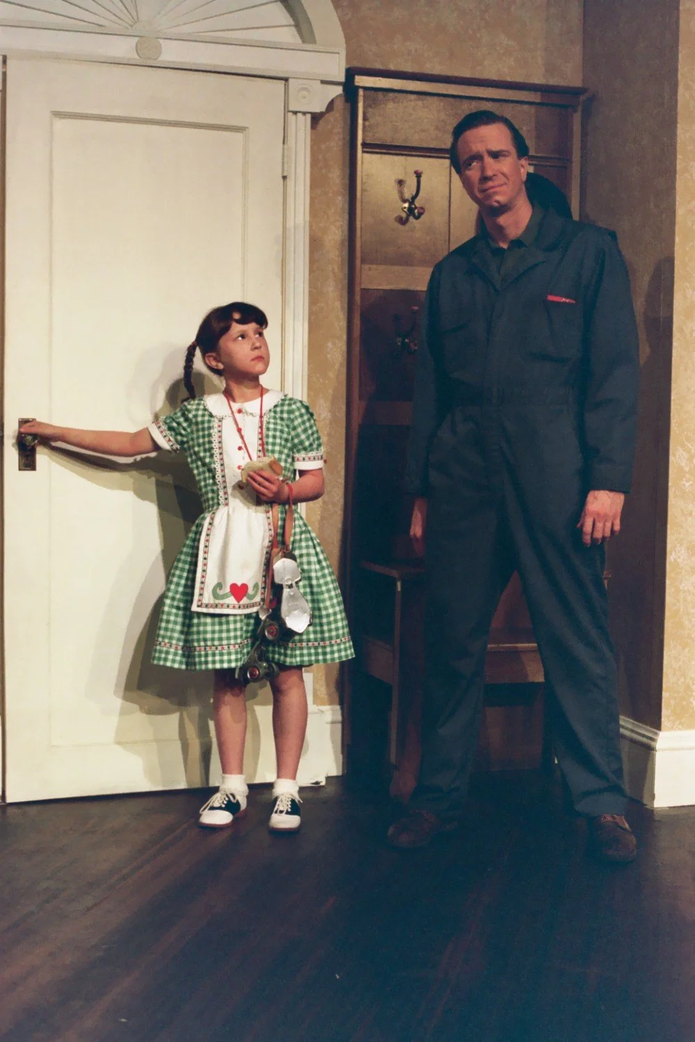 Child in green plaid dress and man in overalls in front of a door.