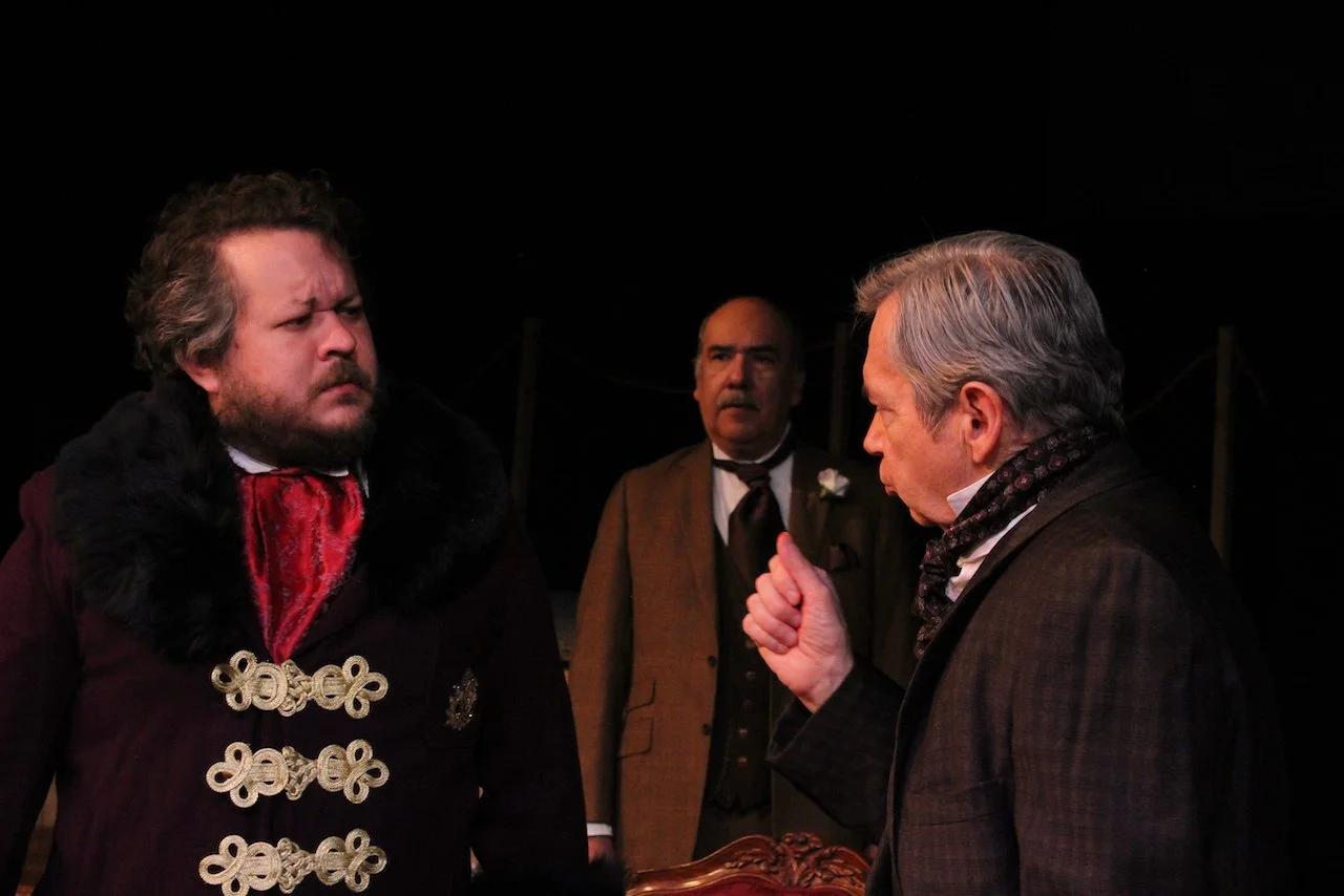 Three men in period costumes performing in a theater play, one gesturing emphatically.