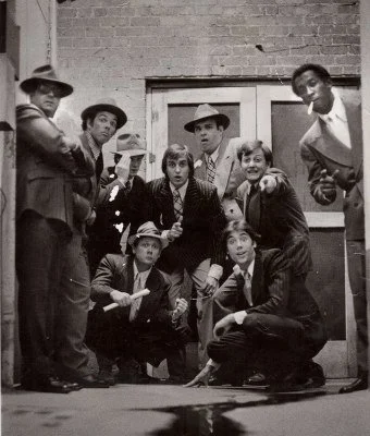 Group of people in vintage suits posing in a noir-style setting.