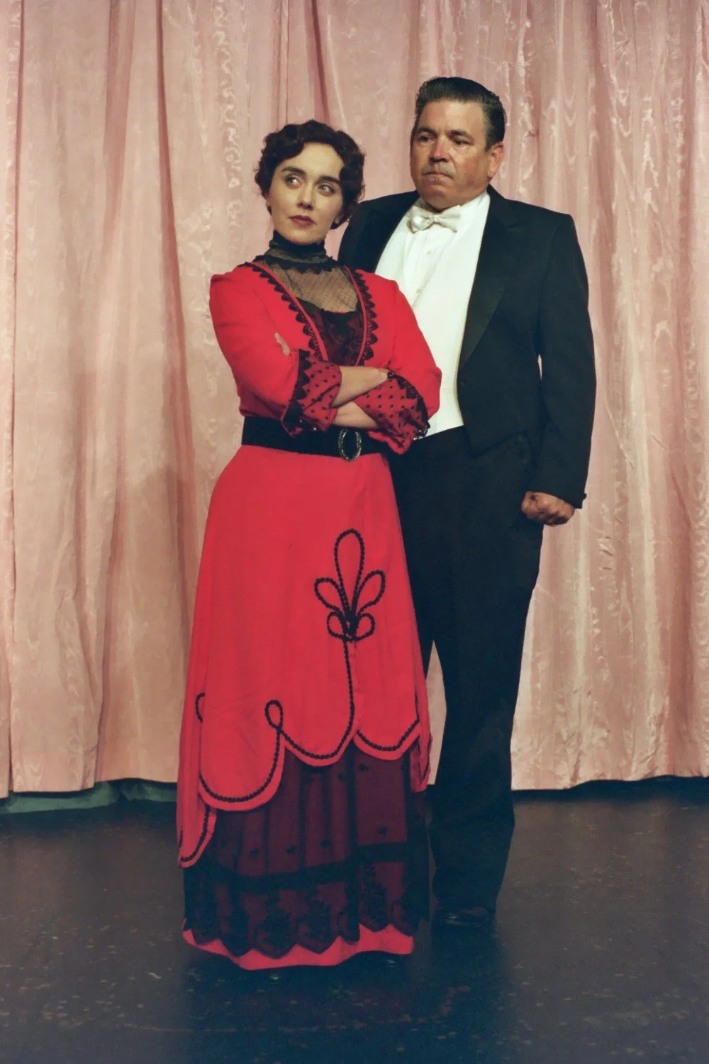 A woman in a red dress and a man in a suit posing in front of pink curtains.