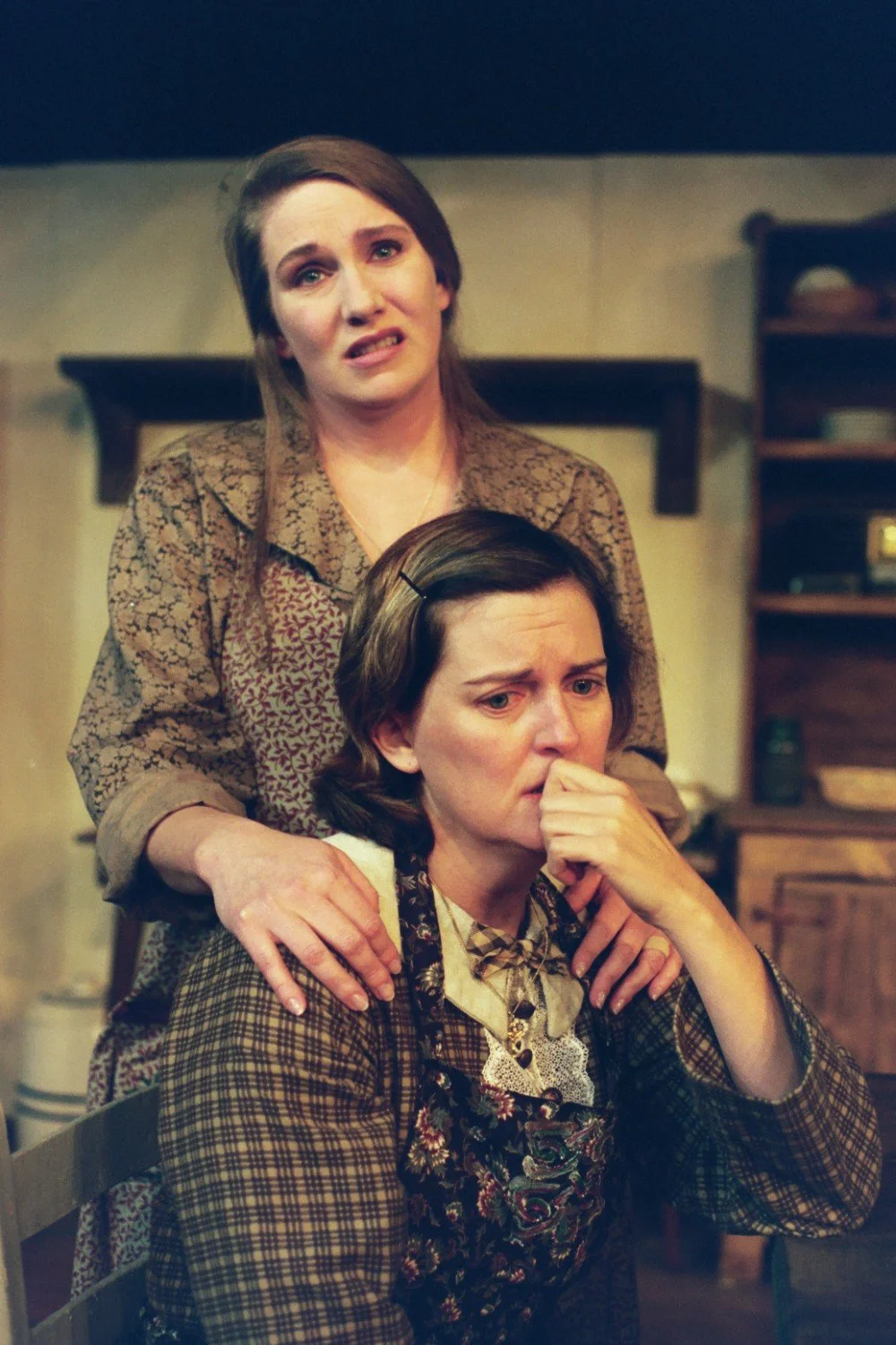 Two women in a vintage setting, one comforting the other.