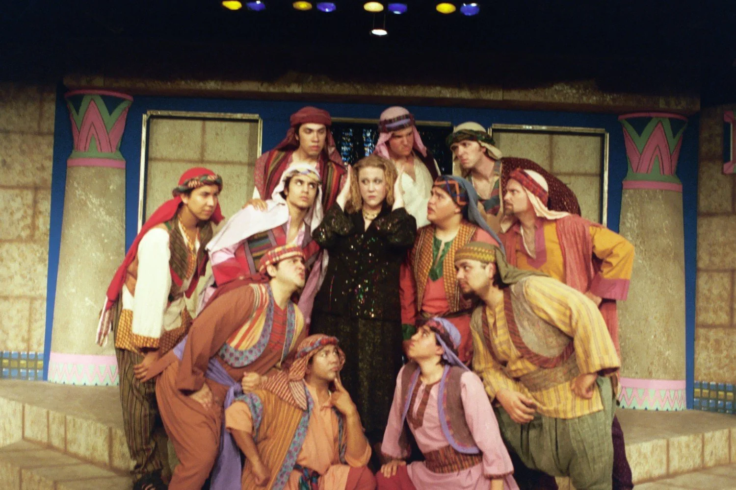 Theatrical performance with cast in colorful clothing and headpieces on stage.