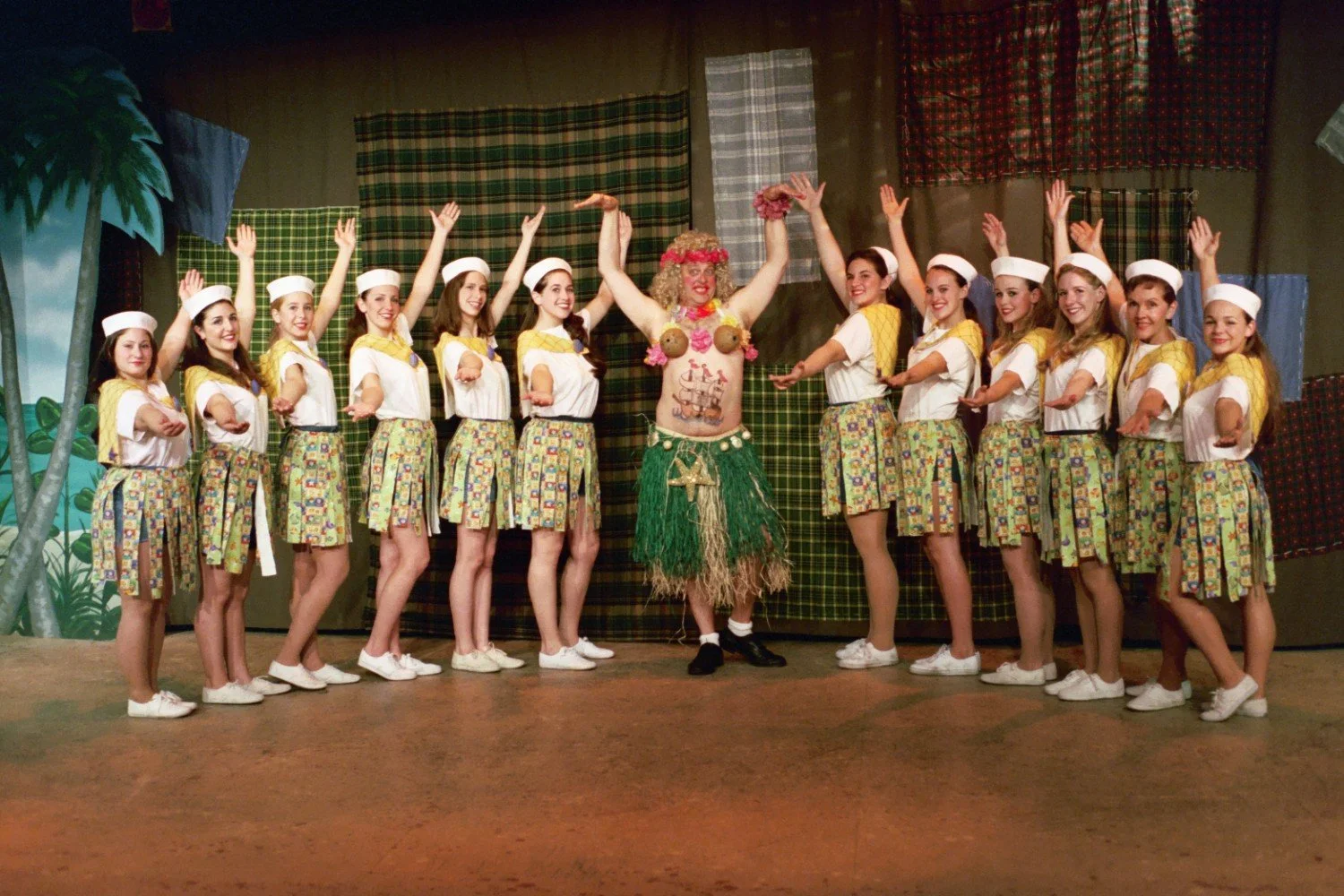 Group of performers in sailor-themed costumes and a person in a hula skirt on stage