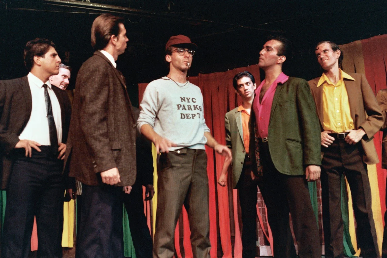 Group of men in suits and casual clothes on stage with colorful curtains