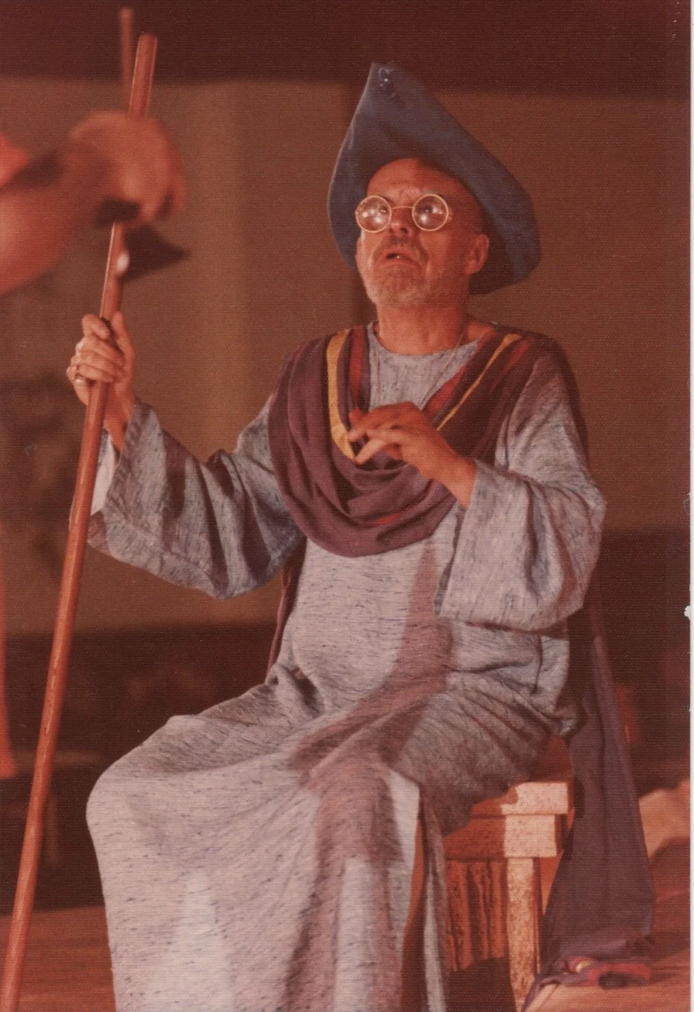 Person in medieval costume with hat and glasses holding a staff