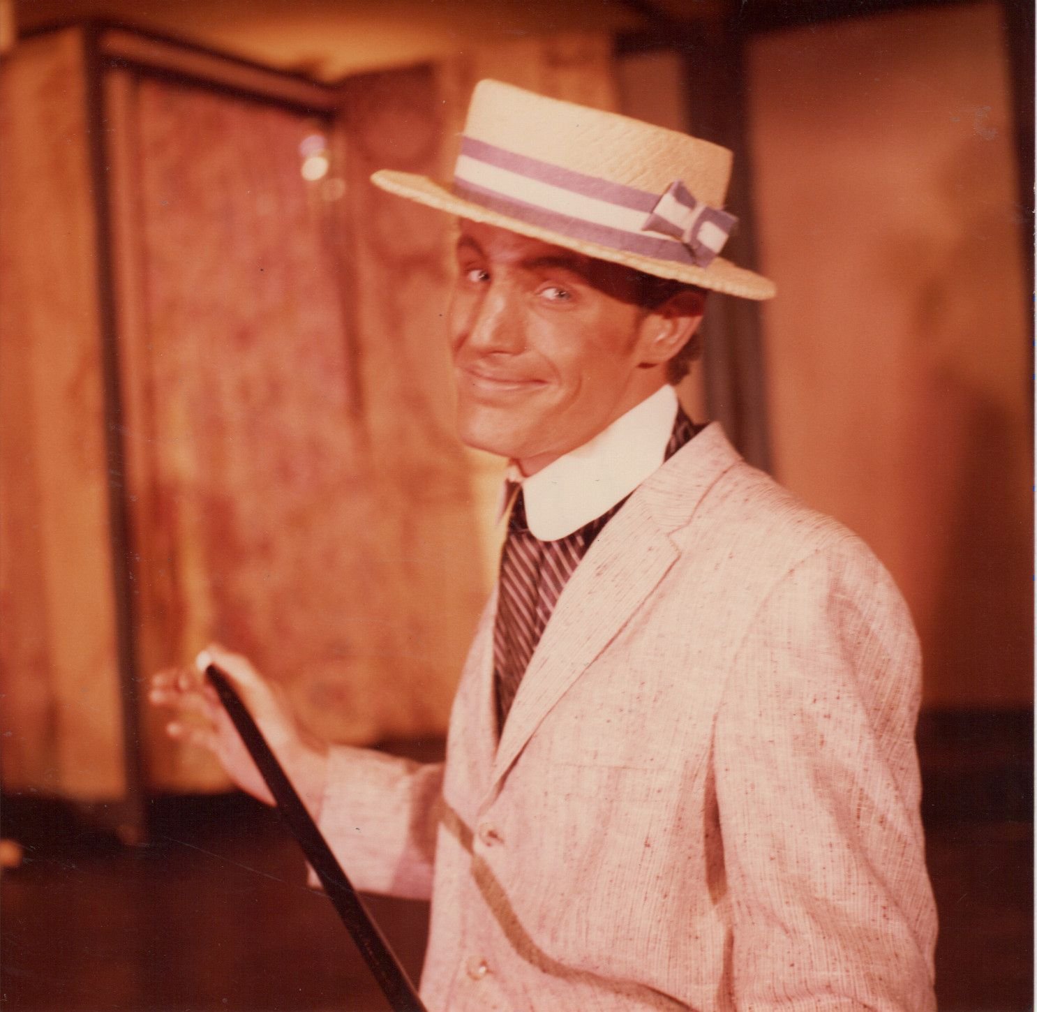 Man in vintage suit and straw boater hat holding a cane, smiling.