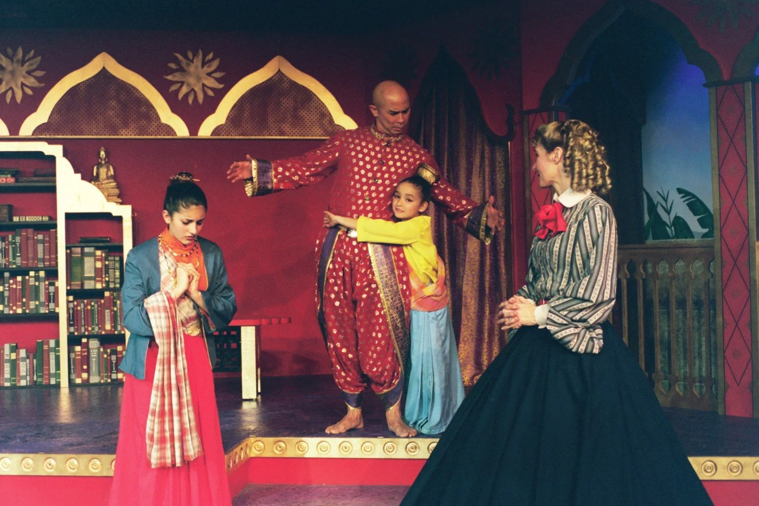 Theatrical performance with four actors in period costumes, depicting a historical or cultural scene on stage with ornate backdrop.