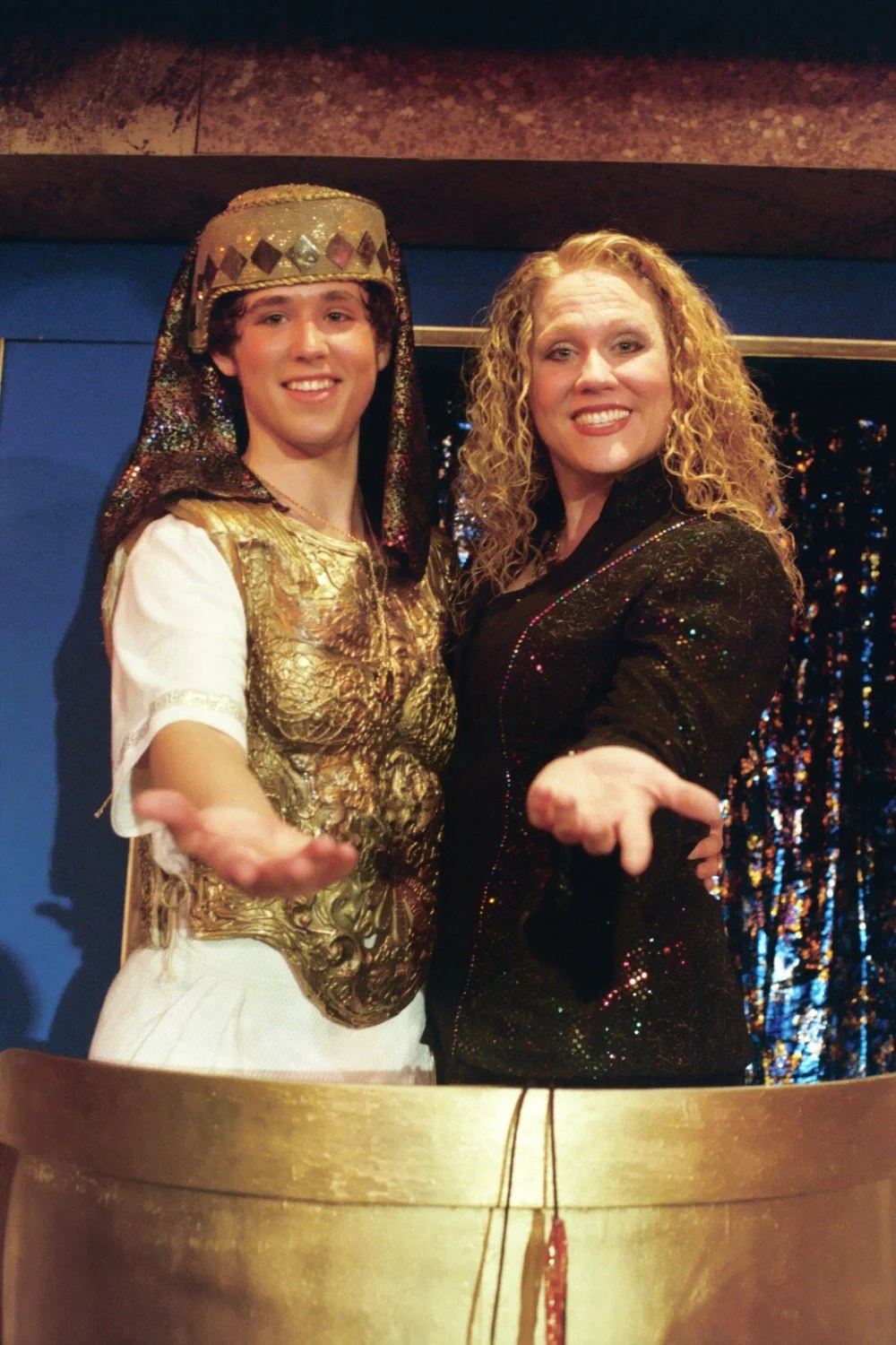 Two performers in colorful costumes posing together on stage, smiling.