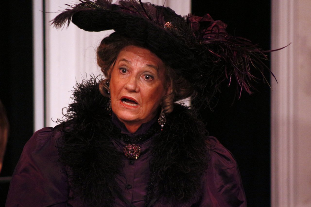 Woman in vintage costume with hat, feather accents, and ornate collar.