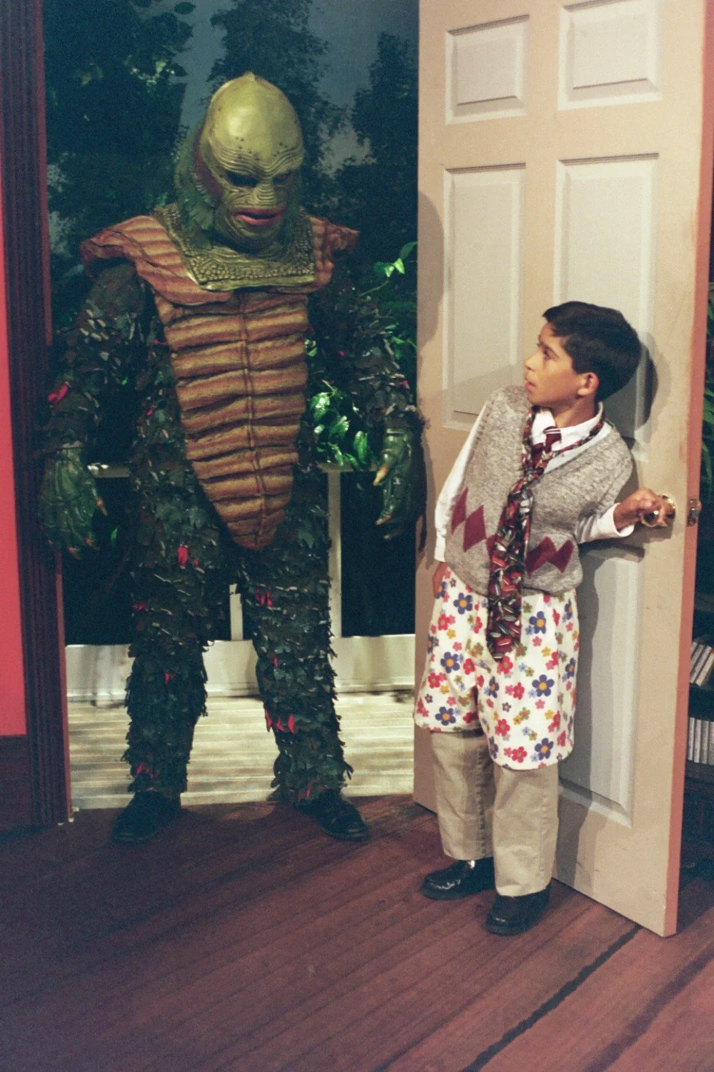Child in mismatched clothing surprised by person in monster costume standing in doorway.