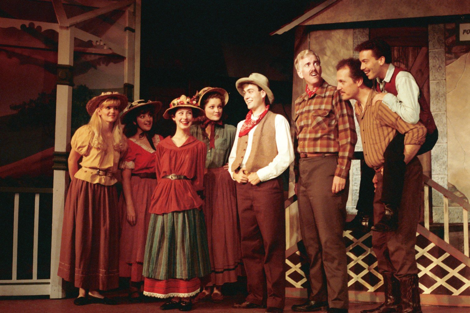 Group of people in cowboy and prairie costumes, smiling and standing together on stage.
