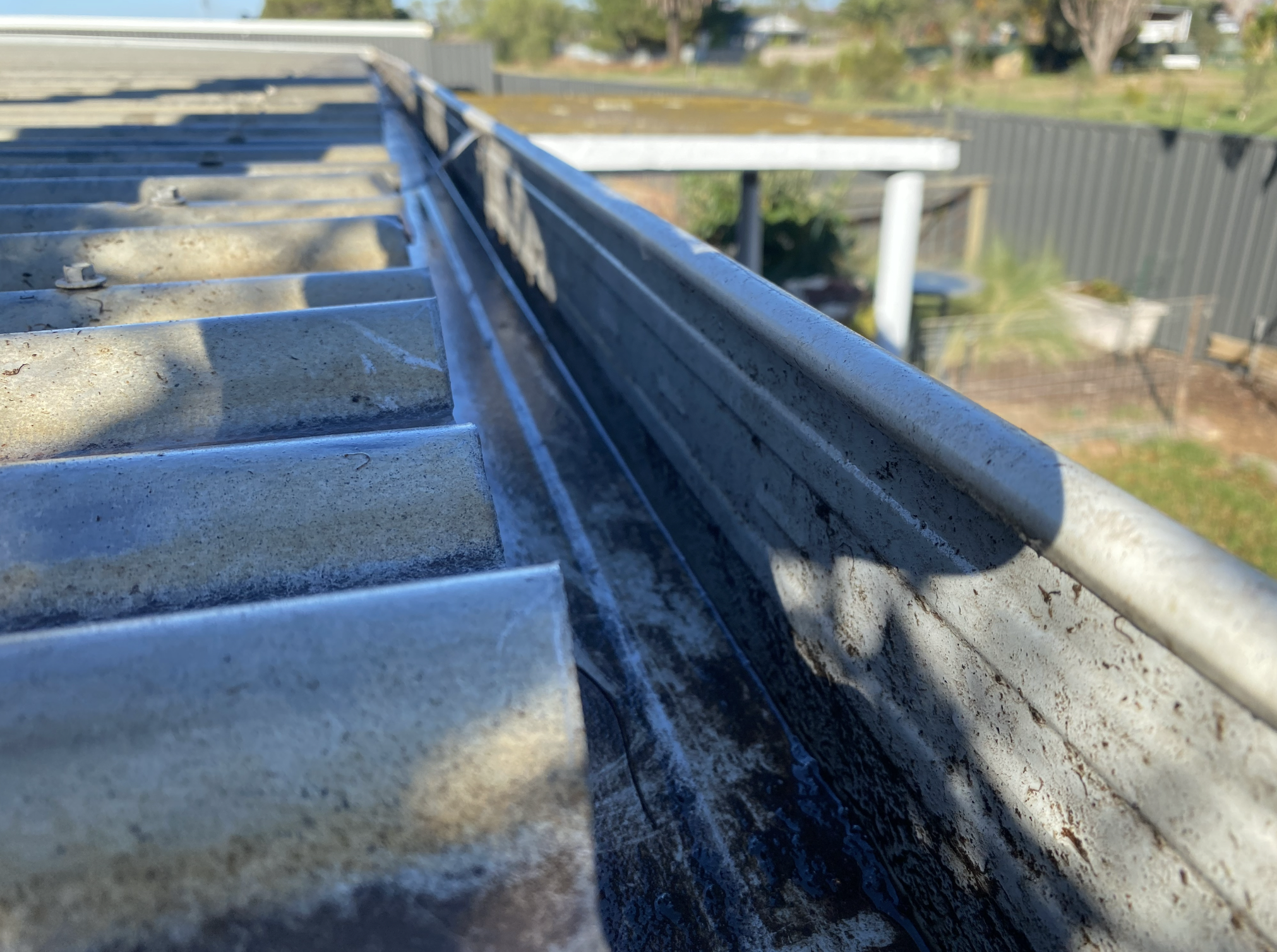 Close-up of a metal roof edge with metal siding underneath, casting a shadow on the surface, outdoors during the daytime.