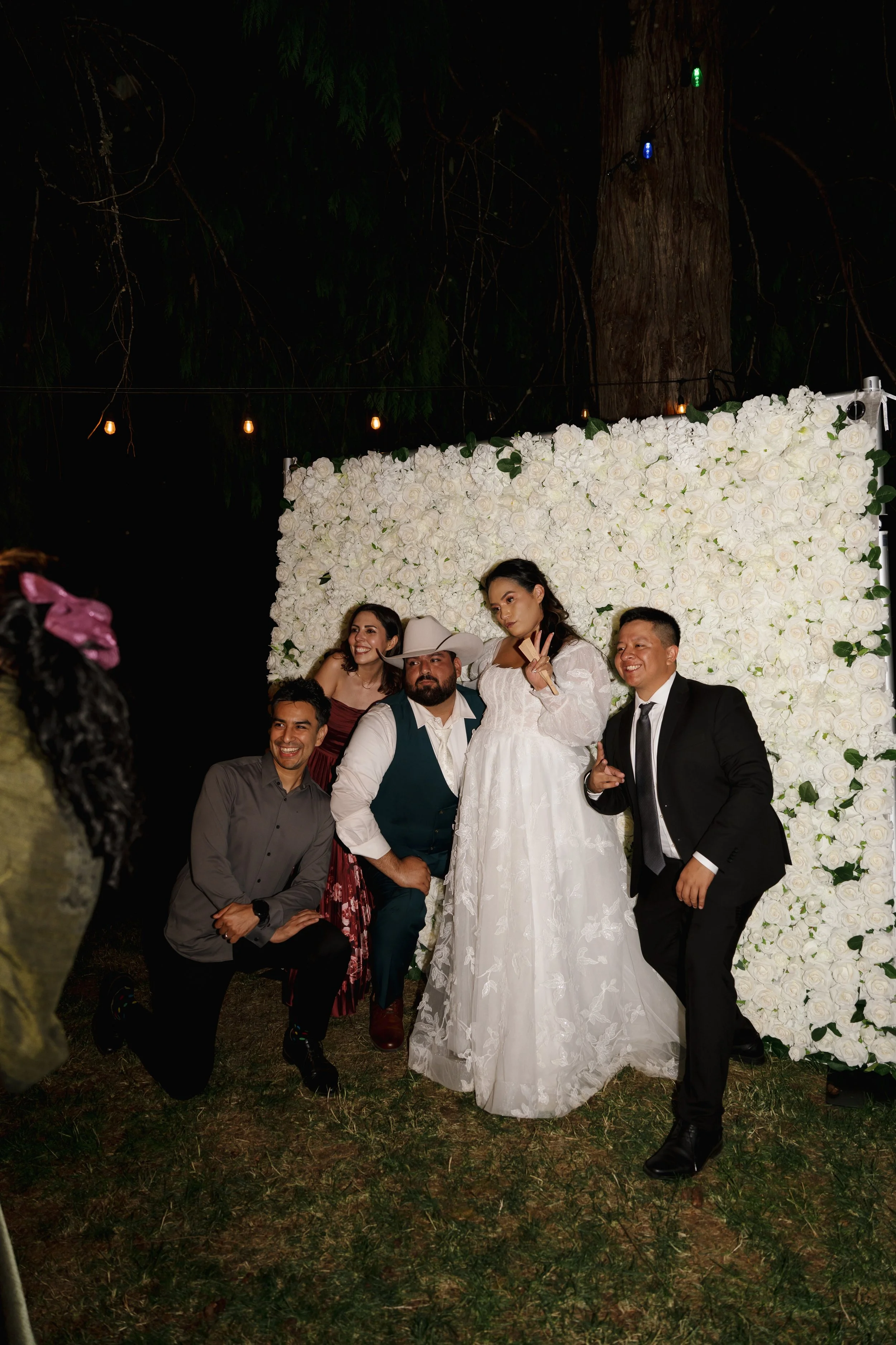 Friends and wedding couple posing in front of flower wall for wedding photo booth.
