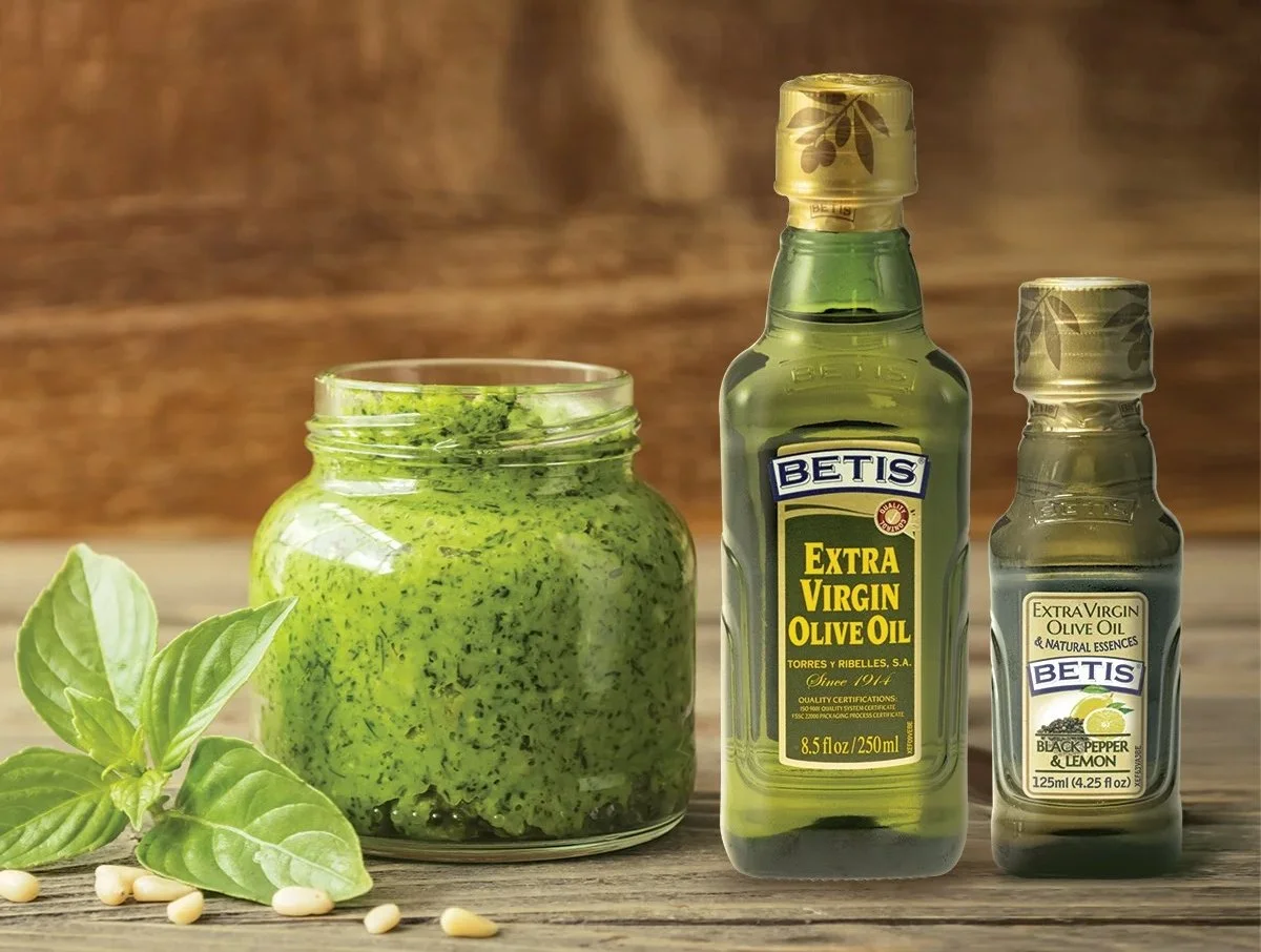 Glass jar of green pesto with basil, pine nuts, and Betis extra virgin olive oil bottles on wooden surface – imported Mediterranean foods supplied by Jetha Australian food importers