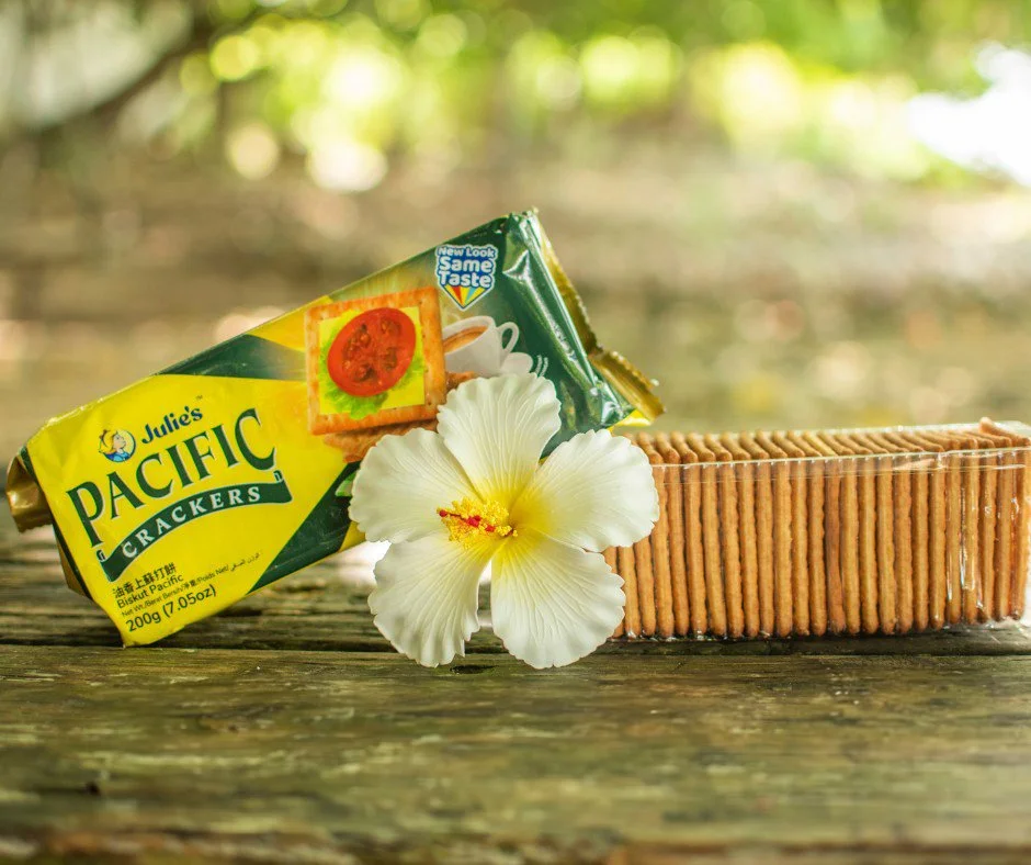 Package of Jules' Pacific Crackers with stacked crackers and white hibiscus flower on wooden surface – imported biscuits supplied by Jetha Australian food importers