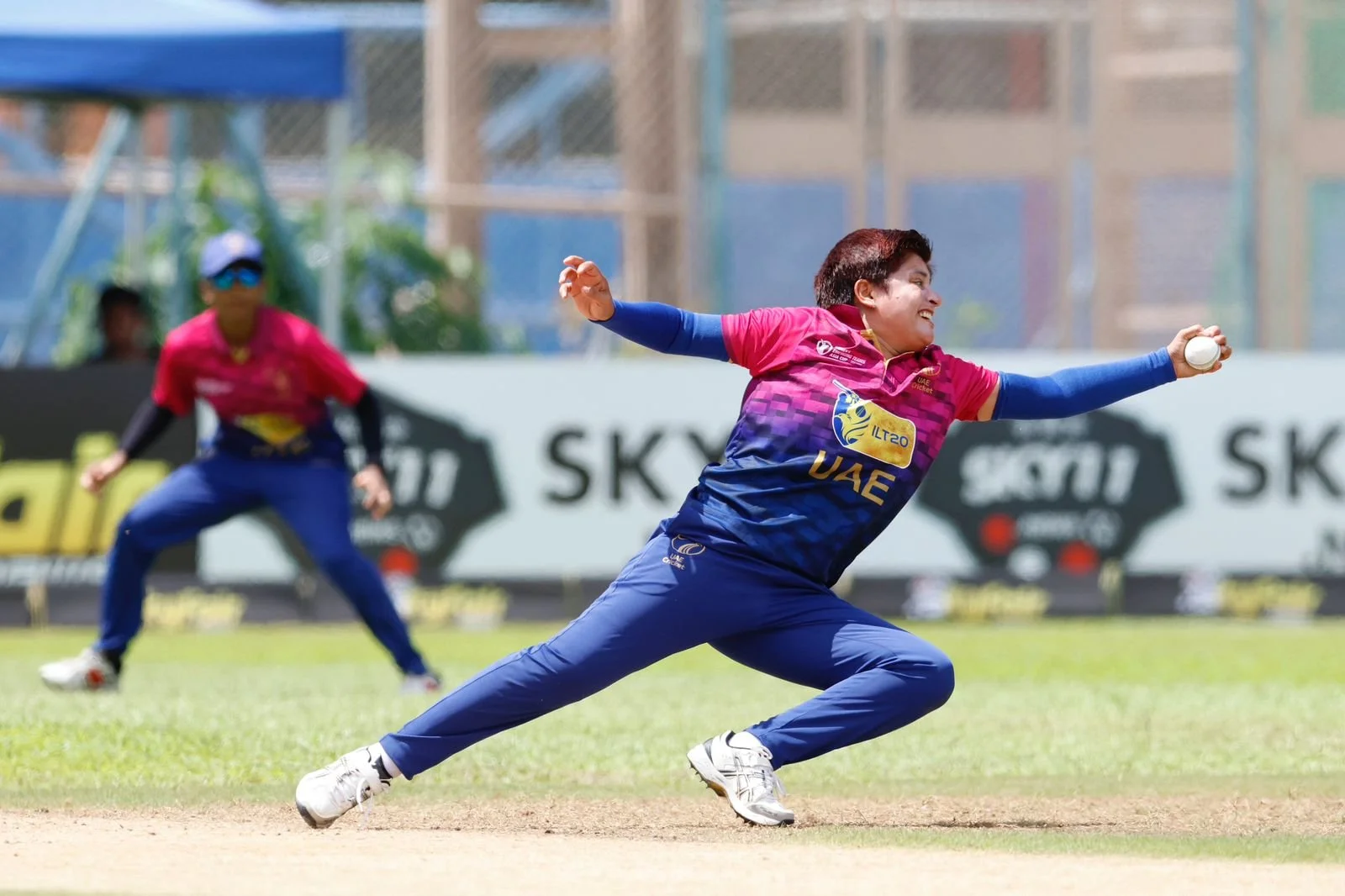 Chaya Mughal - a woamn on a cricket pitch reaching to catch a ball
