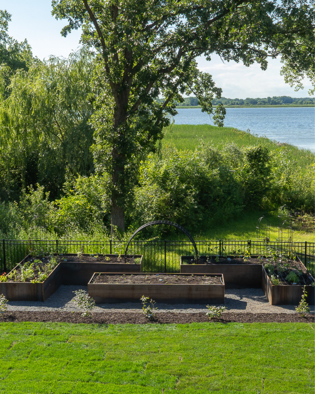 Lakeview potager garden with custom corten steel raised beds, an arch trellis, and gray stone pathways overlooking the water.
