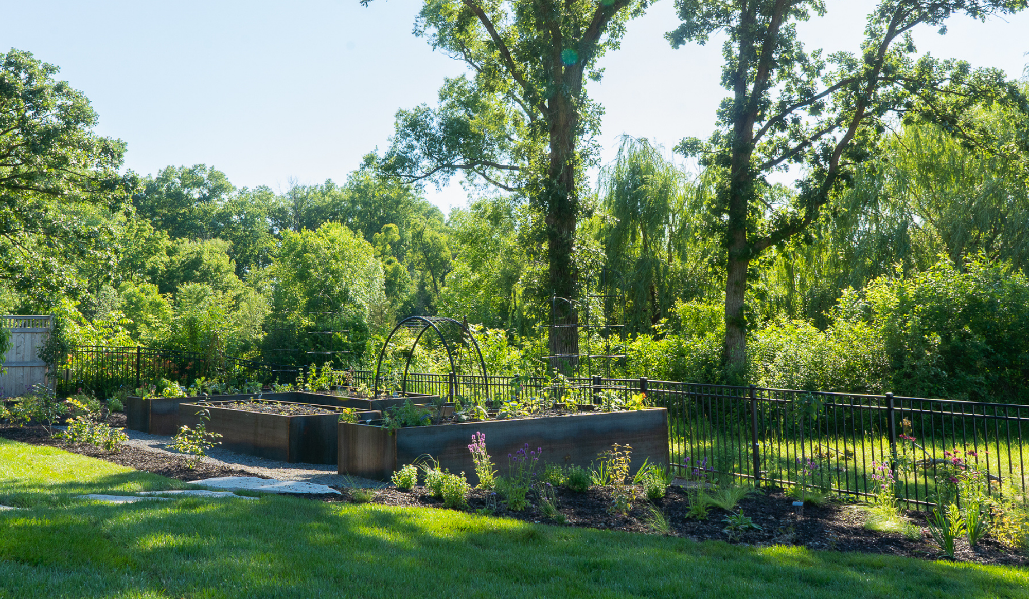 Corten steel raised bed kitchen garden surrounded by lush perennial plantings and mature trees in Trevor, Wisconsin.