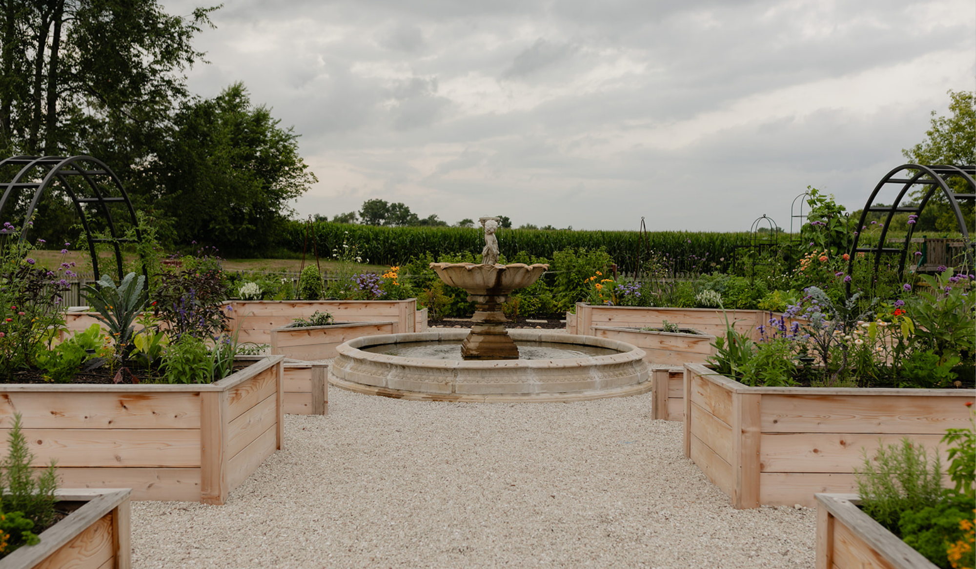 Formal potager garden at LaRocque Farms with a central fountain framed by cedar raised beds, flowers, and black arch trellises.