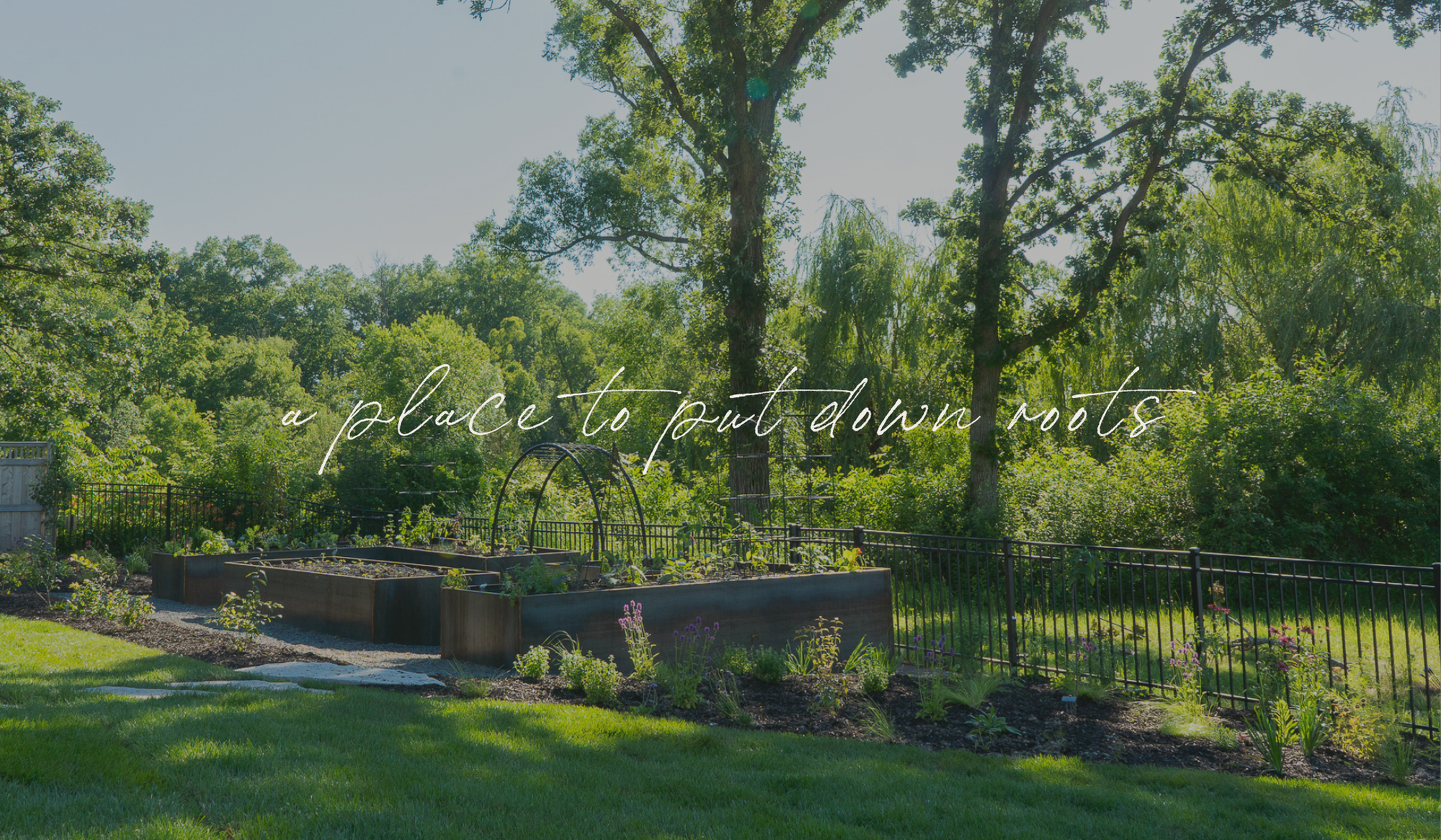 The Rooted Garden surrounded by mature trees and perennial plantings, designed as a place to put down roots.