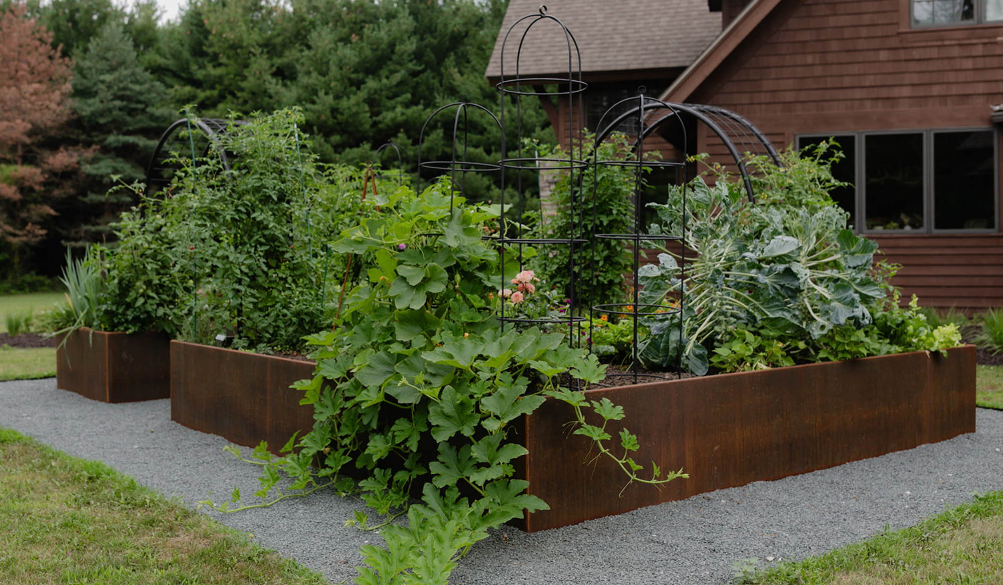 Corten steel kitchen garden with abundant vegetables, black arch trellises, and gray stone pathways in Fontana, Wisconsin.”