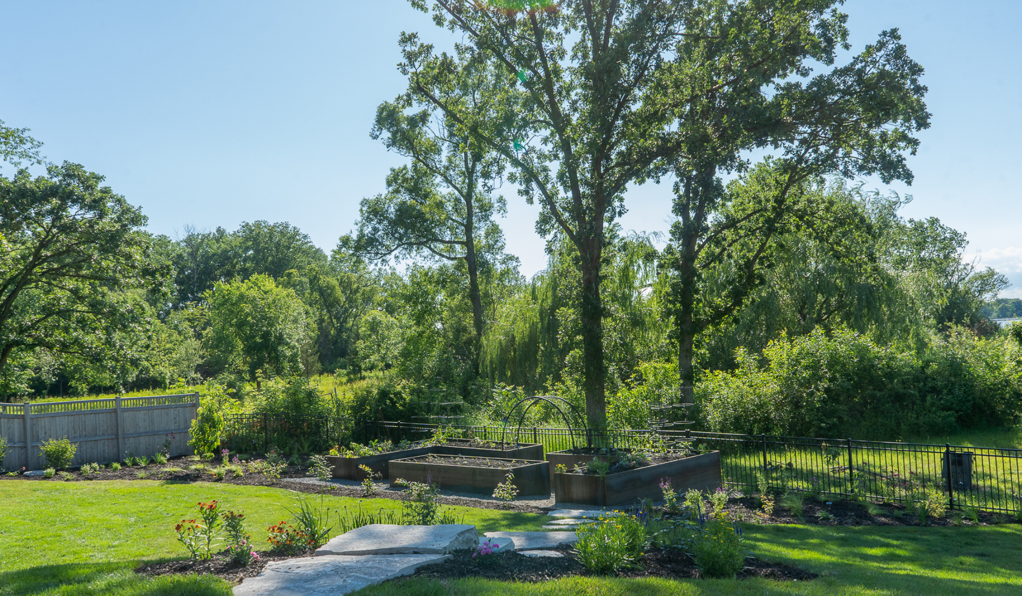 Lakeview kitchen garden with custom corten steel raised beds, trellises, and surrounding plantings overlooking the water.