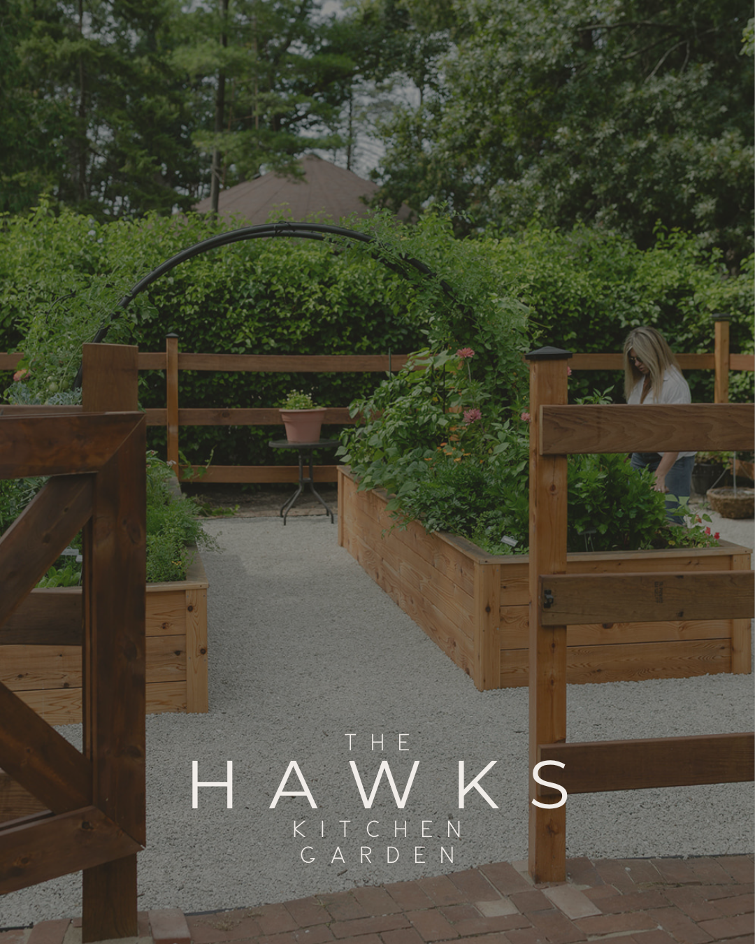 The Hawks Kitchen Garden with cedar raised beds, a custom arch trellis, white gravel pathways, and a gated entrance in Lake Geneva, Wisconsin.