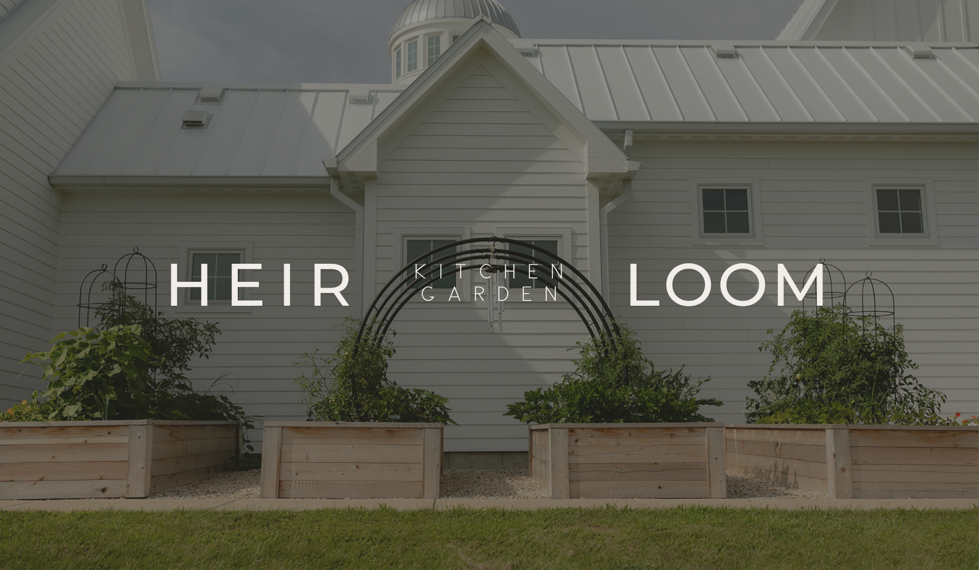 The Heirloom Garden with four cedar raised beds and custom black trellises beside a restored family farmhouse in Harvard, Illinois.
