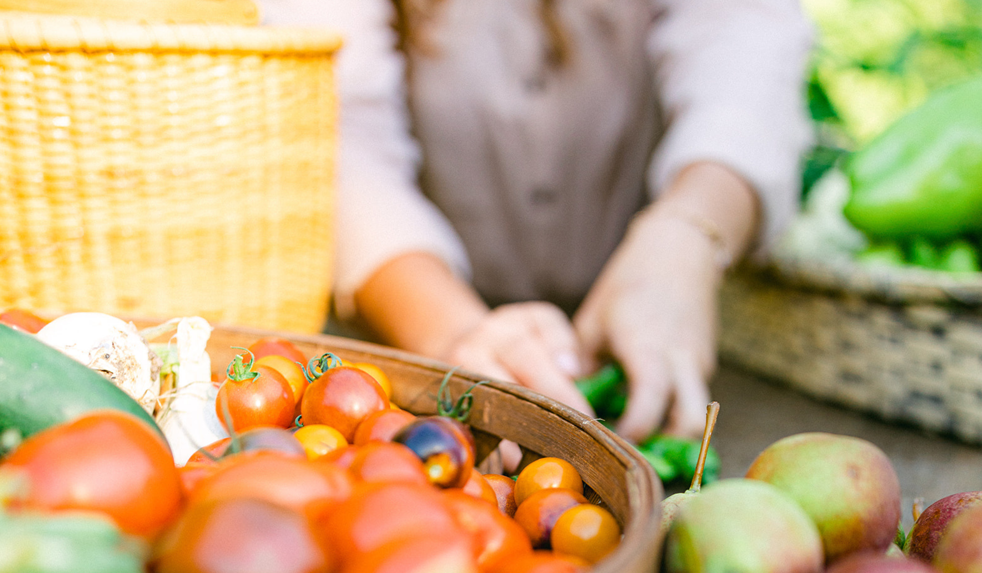 Close-up of a basket filled with colorful heirloom tomatoes, with freshly harvested pears and other garden vegetables on the table.