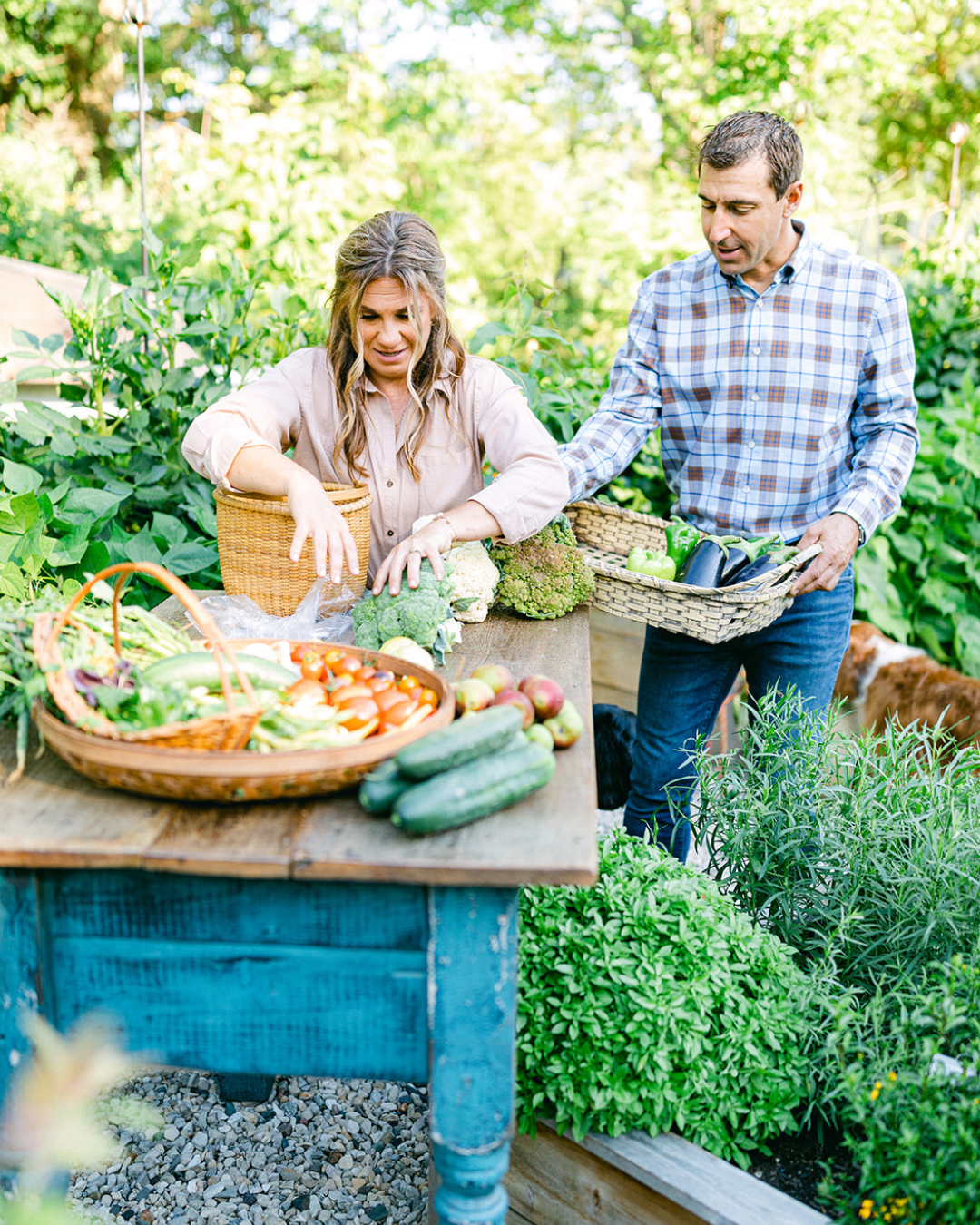 Katie and Matt Oglesby sorting a summer harvest of broccoli, peppers, cucumbers, tomatoes, and other vegetables in their garden.