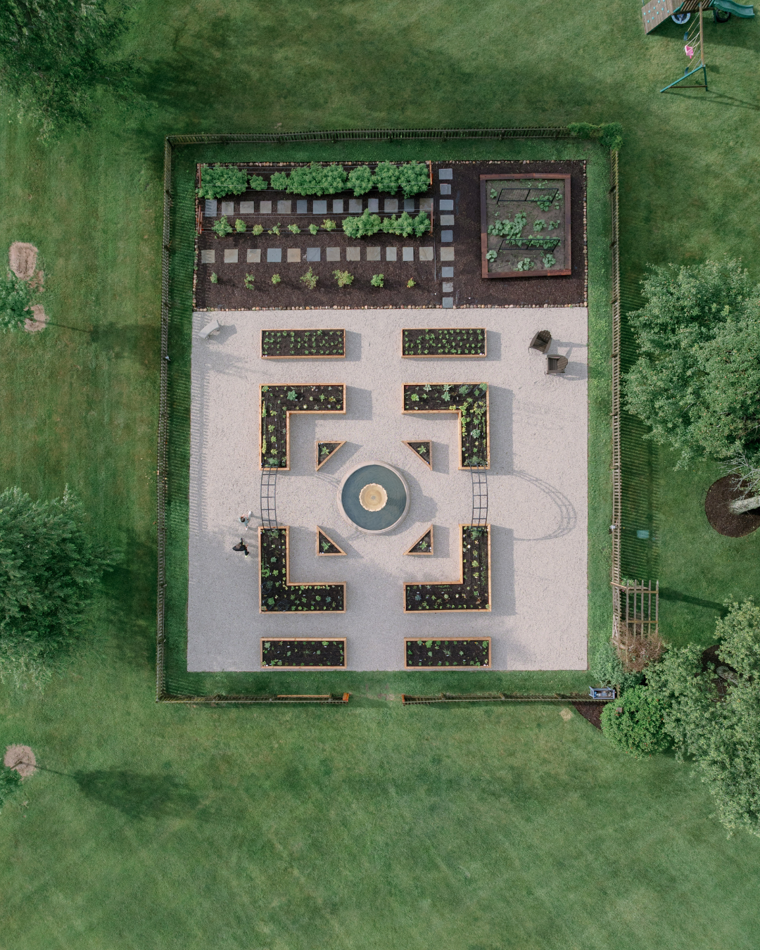 Aerial view of the LaRocque Farms kitchen garden showing the symmetrical potager, central fountain, cedar raised beds, gravel pathways, and adjoining in-ground growing area.