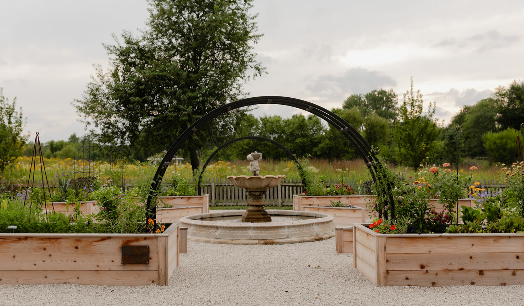 Central fountain framed by a custom black arch trellis and abundant flowers in the LaRocque Farms kitchen garden.