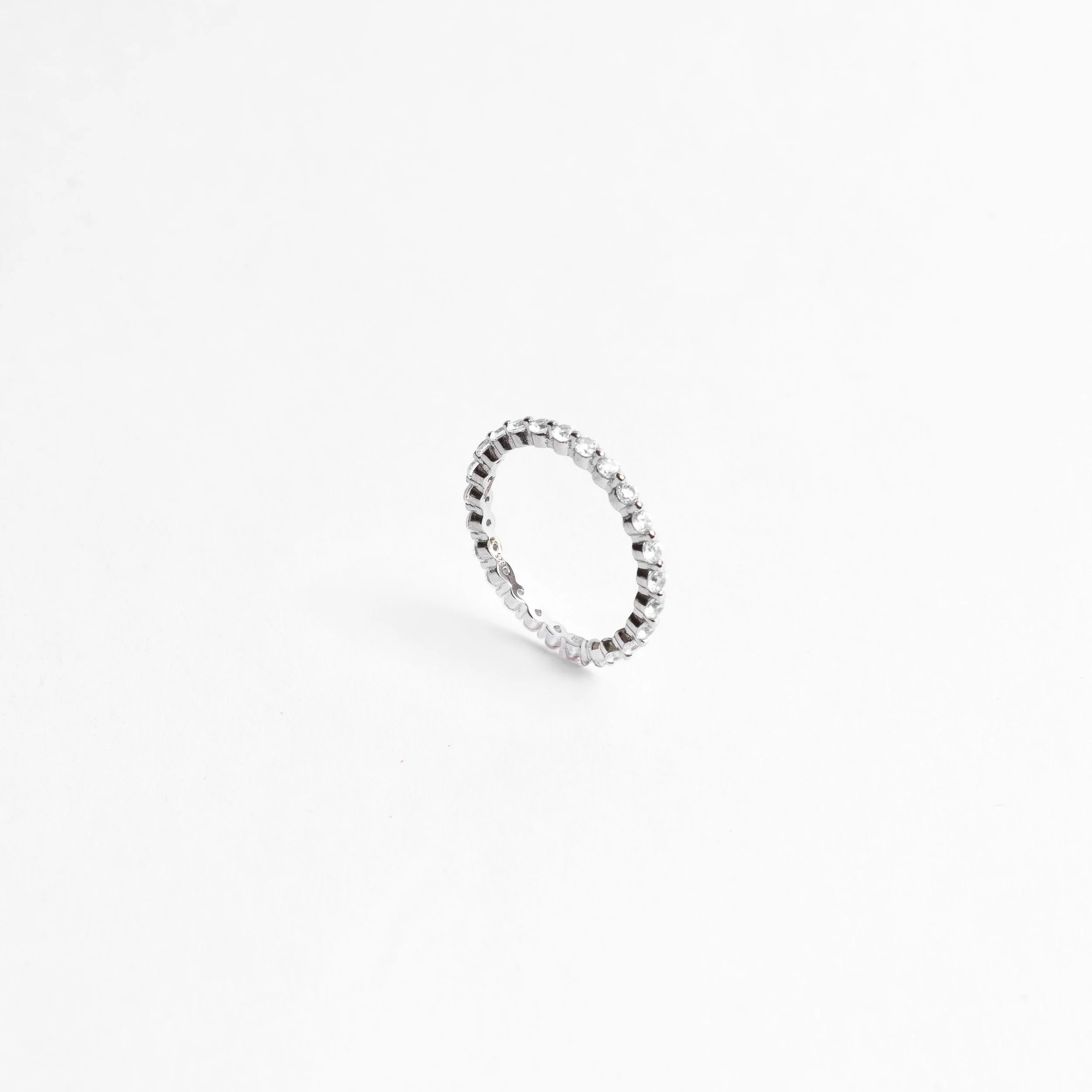 A silver ring with small, evenly spaced gemstones, standing upright on a plain white background.