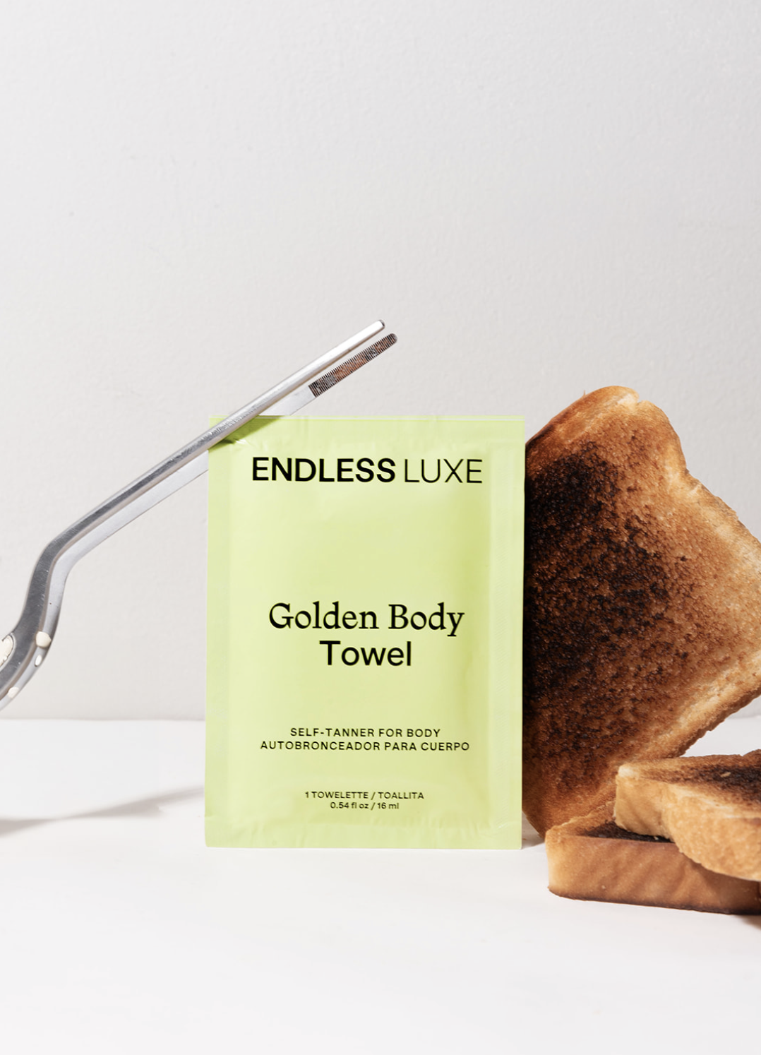 A pack of Endless Luxe Golden Body Towel, a pair of gold-tinted slippers, a razor, and two slices of toasted bread on a white surface.