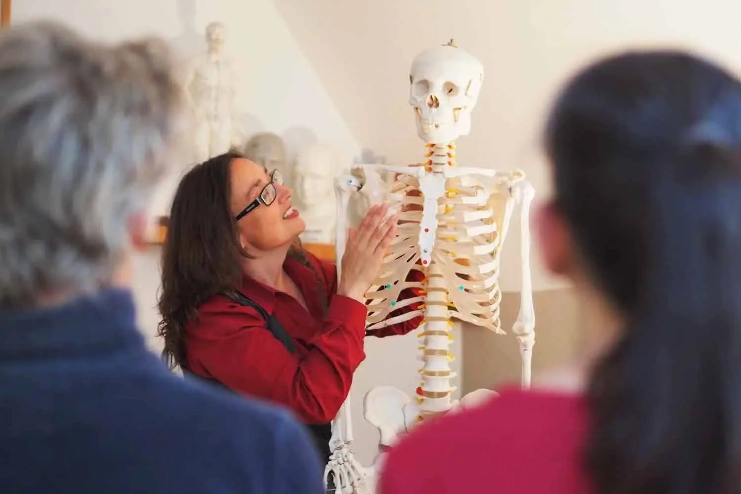 A woman demonstrating a human skeleton model to a small group of people in a classroom setting.