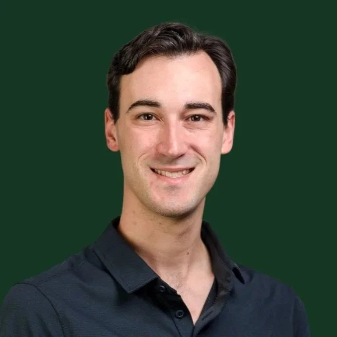 Headshot of a young man with dark hair, smiling, wearing a dark button-up shirt, against a solid green background.