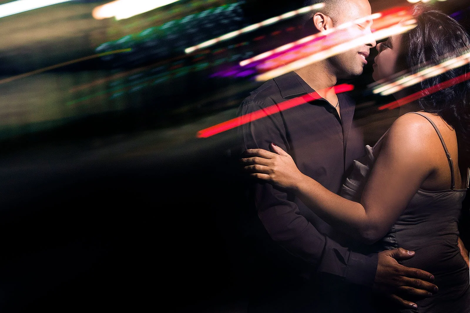 A couple holding each other close in a dark setting with colorful light streaks across the image.