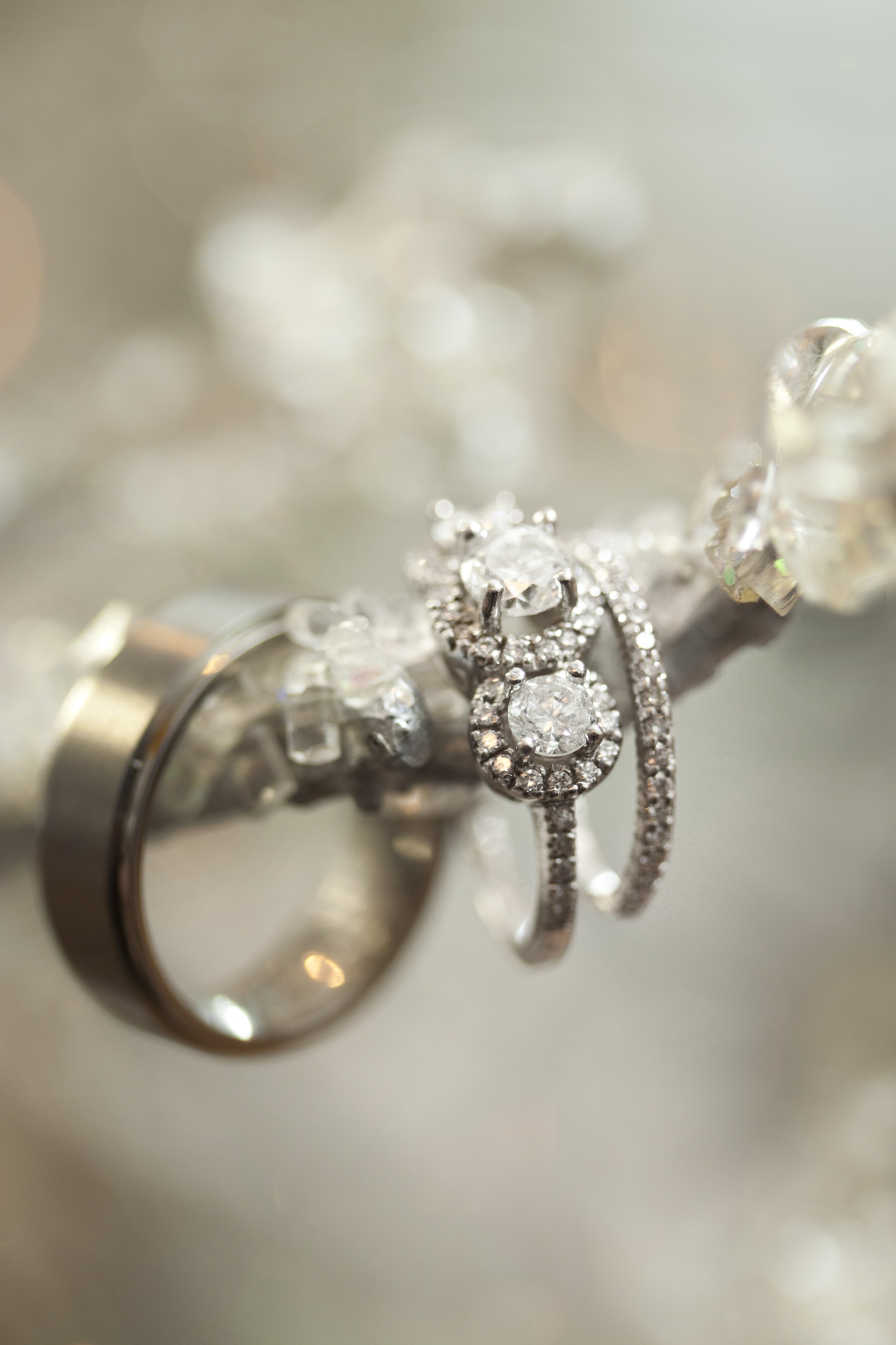 Close-up of silver jewelry, including rings and earrings, adorned with sparkling diamonds, placed on a shiny silver surface.