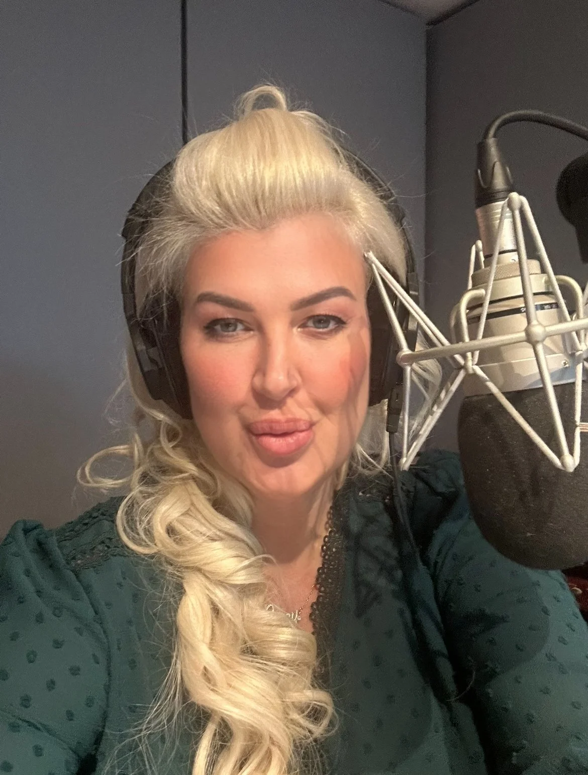 A woman with blonde hair recording in a professional studio with a microphone and headphones.