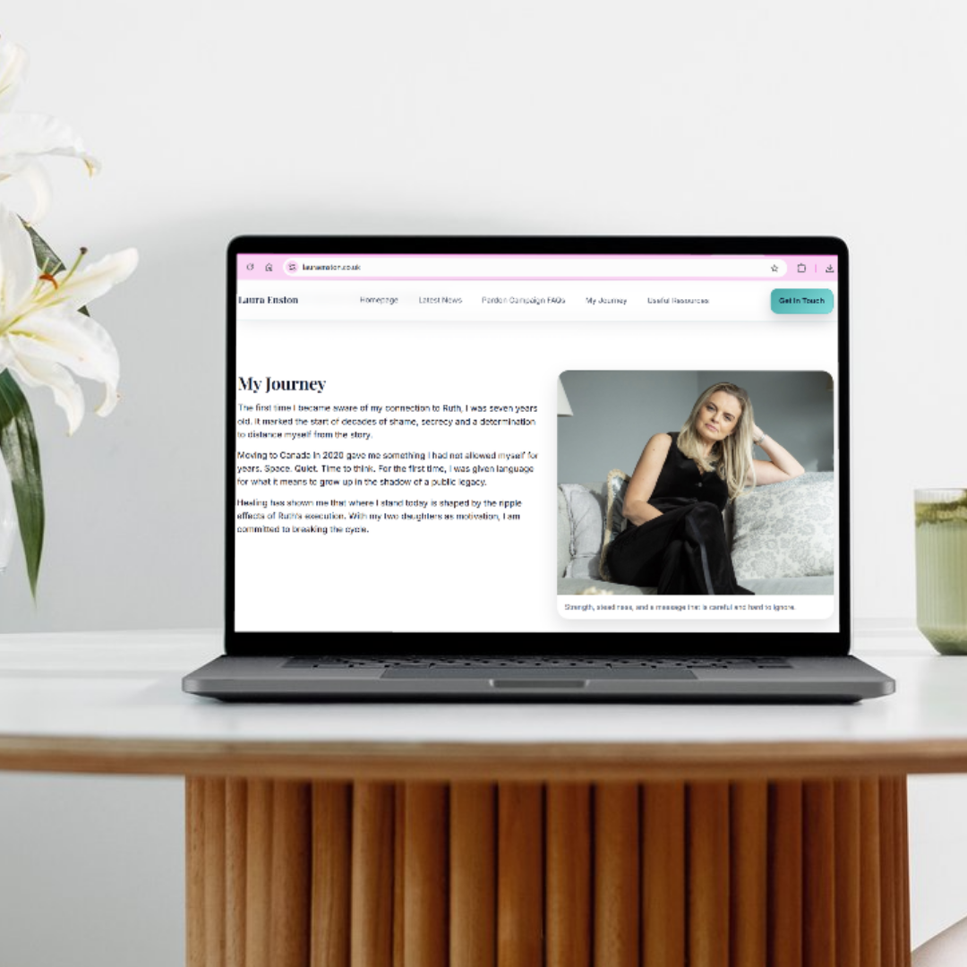 Laptop on a wooden desk displaying a personal web page with a photo of a woman sitting on a sofa, two white lilies in a green vase on the left, and a potted plant on the right.